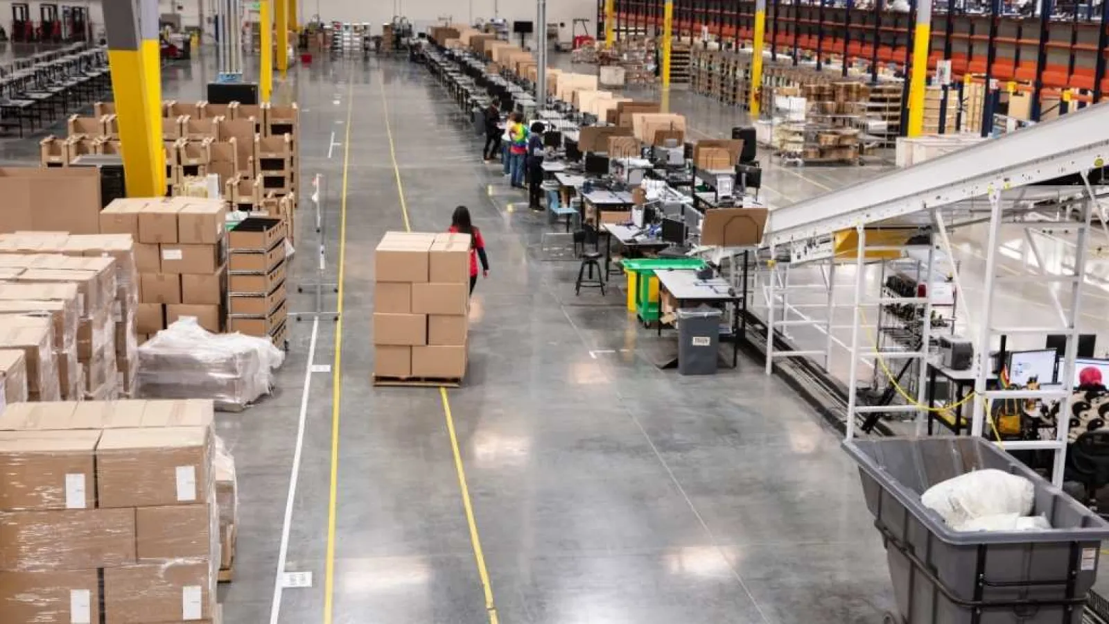 Warehouse interior with workers, conveyor belts, and stacked boxes on pallets in a spacious industrial facility