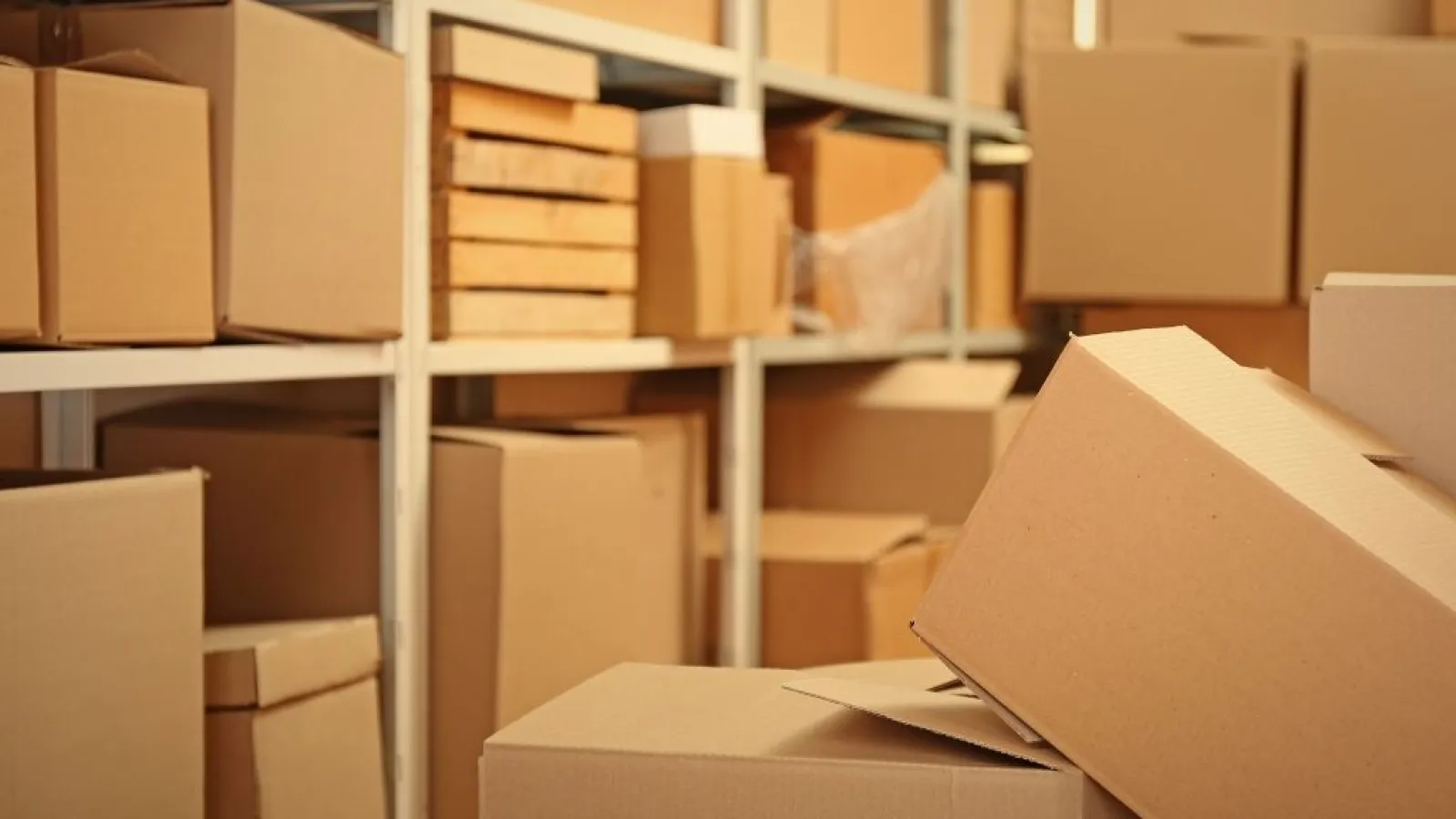 Shelves filled with various sizes of stacked brown cardboard boxes in a storage room or warehouse.