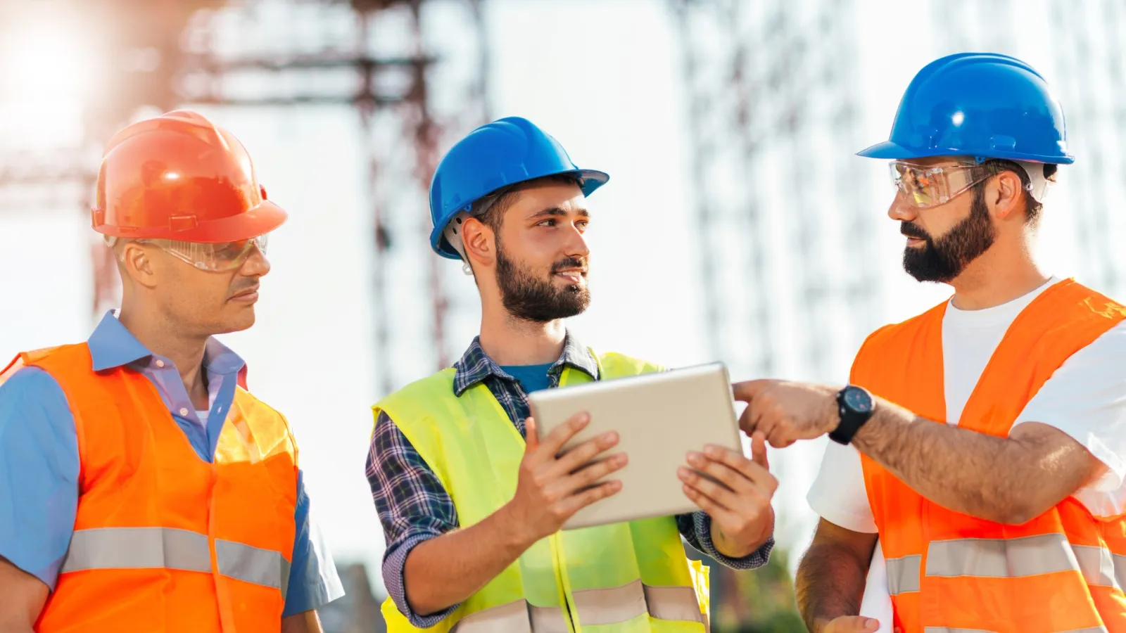a group of men wearing hardhats and reflectors looking at a tablet