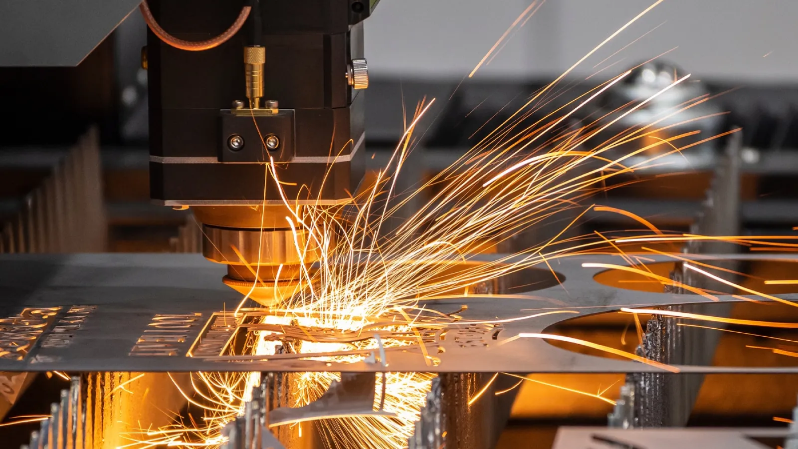 Close-up of industrial laser cutting metal sheet with bright sparks flying in manufacturing workshop