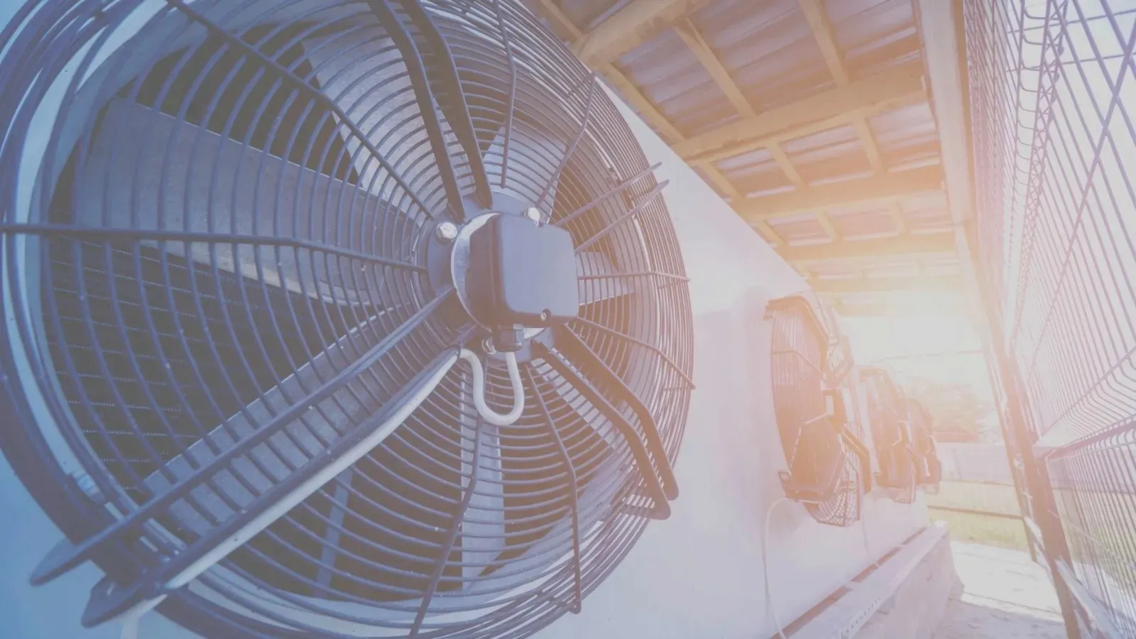 Close-up of industrial outdoor cooling fans on a rooftop with bright sunlight in the background