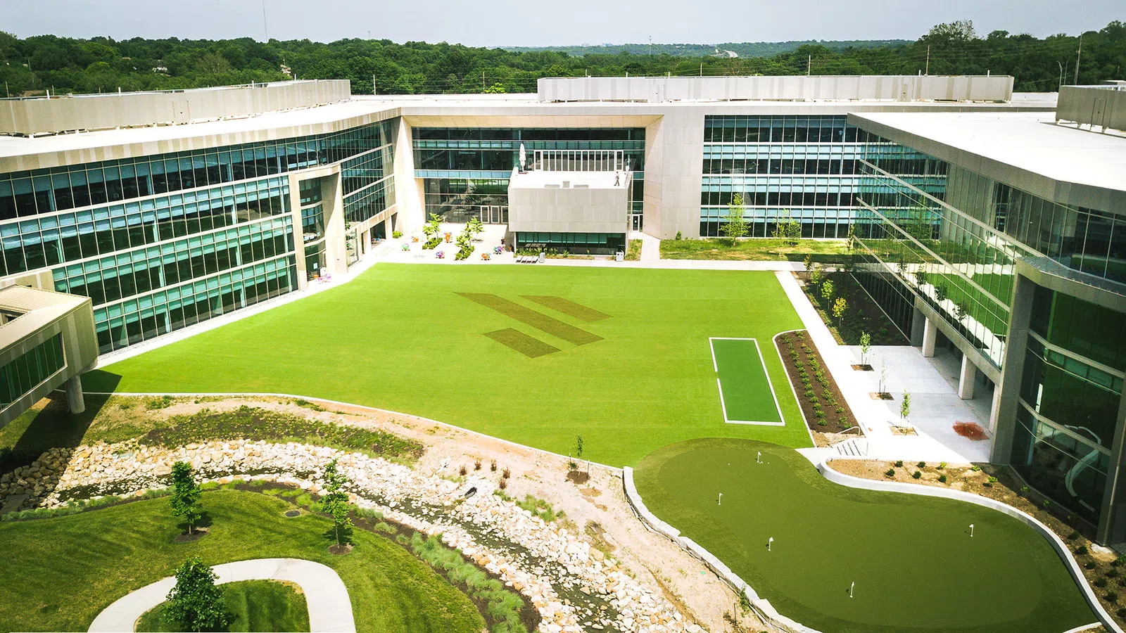 Modern office complex with large green lawn, landscaped garden, and putting green surrounded by glass buildings.