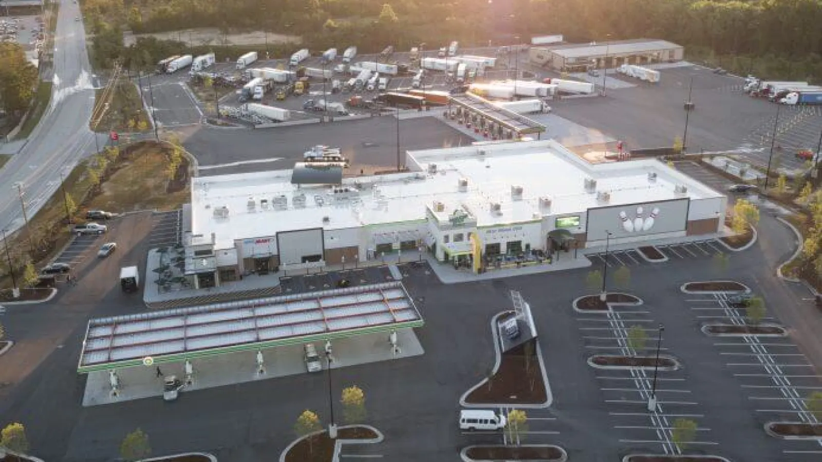 Aerial view of a large truck stop with fueling stations and parking areas surrounded by trees and roads.