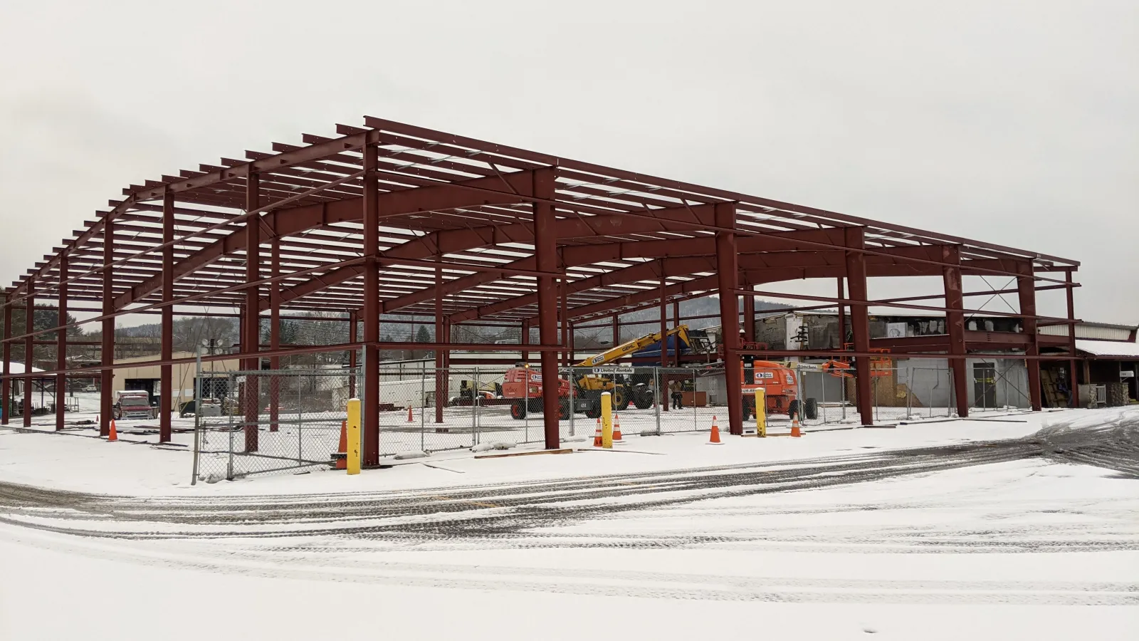 Steel frame structure of a building under construction in a snowy landscape with construction equipment inside.