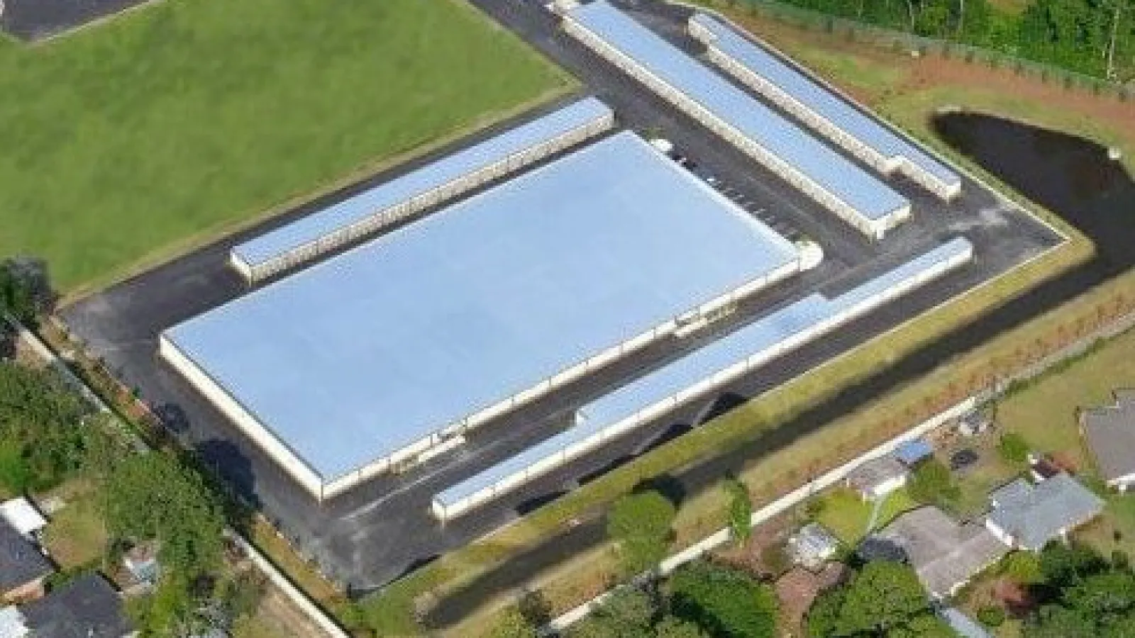 Aerial view of a large industrial warehouse with adjacent smaller buildings and surrounding greenery.
