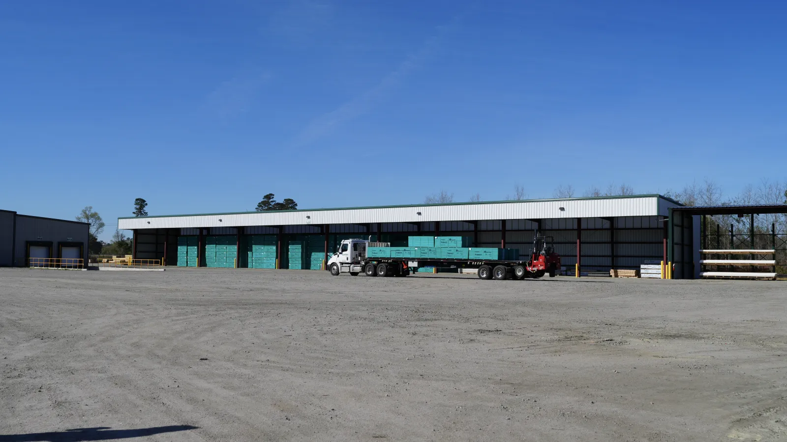 Aerial view of a large warehouse with stacks of materials stored under a metal roof and on concrete pavement.