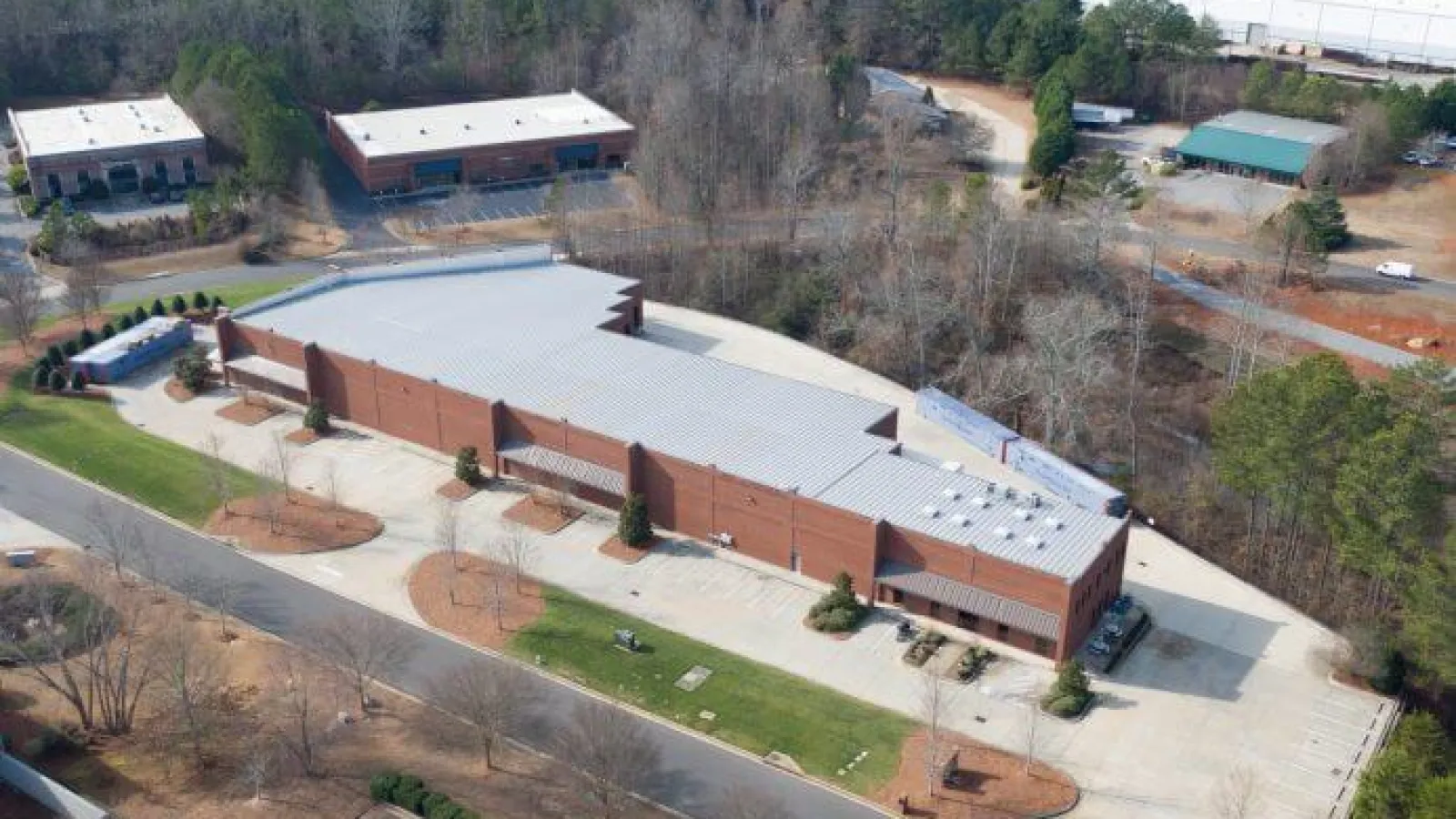 Aerial view of a large brick commercial building with a gray metal roof surrounded by parking lots and trees.