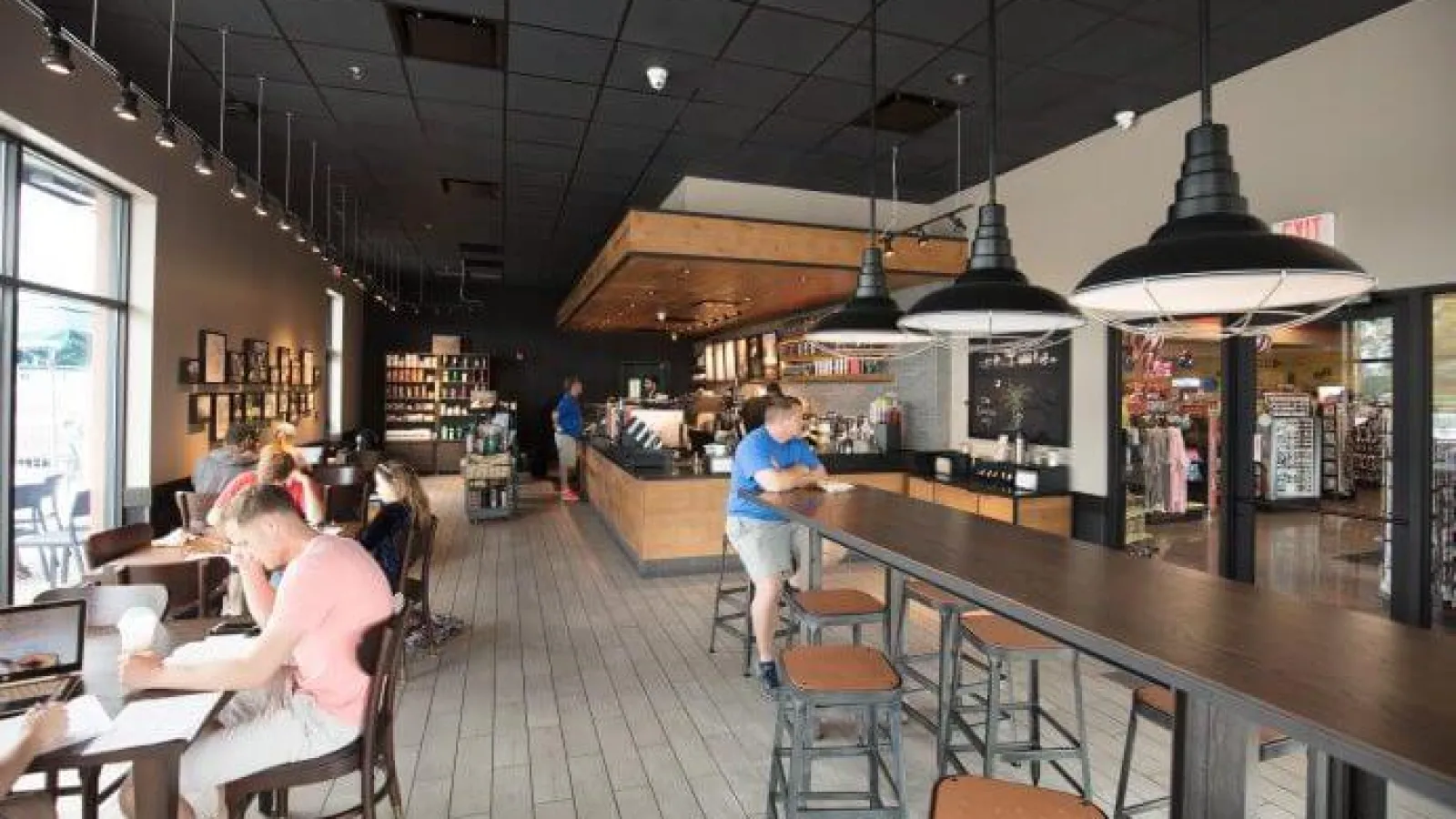 Modern industrial warehouse building with parking lot, cars, trees, and clear blue sky in daytime.