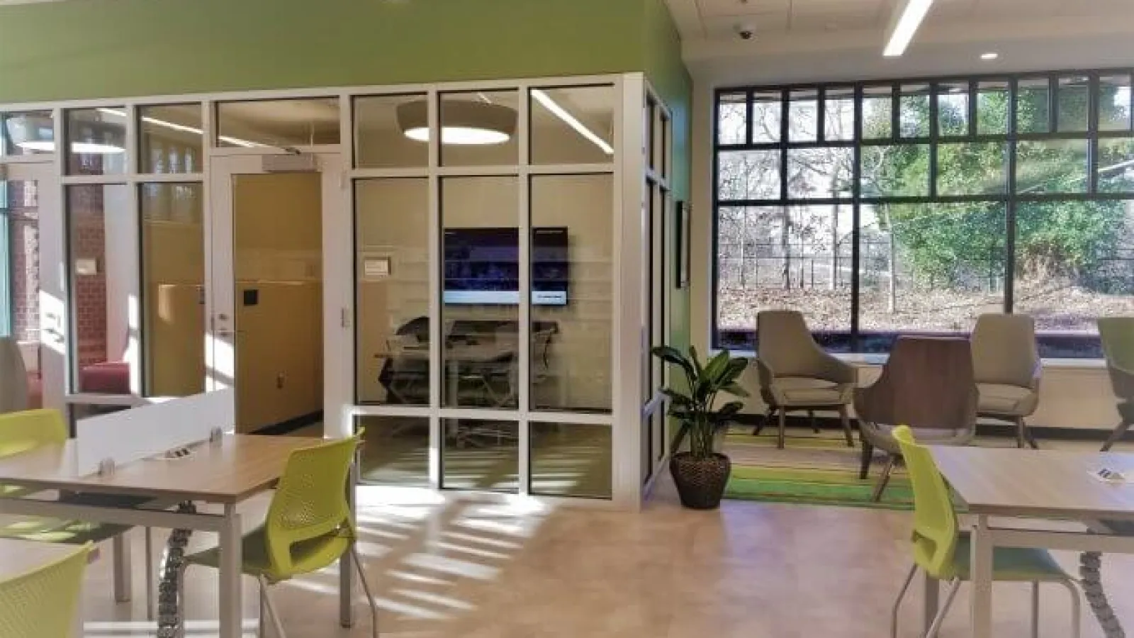 Modern office space with glass-walled meeting room, green chairs, large window, and natural light.