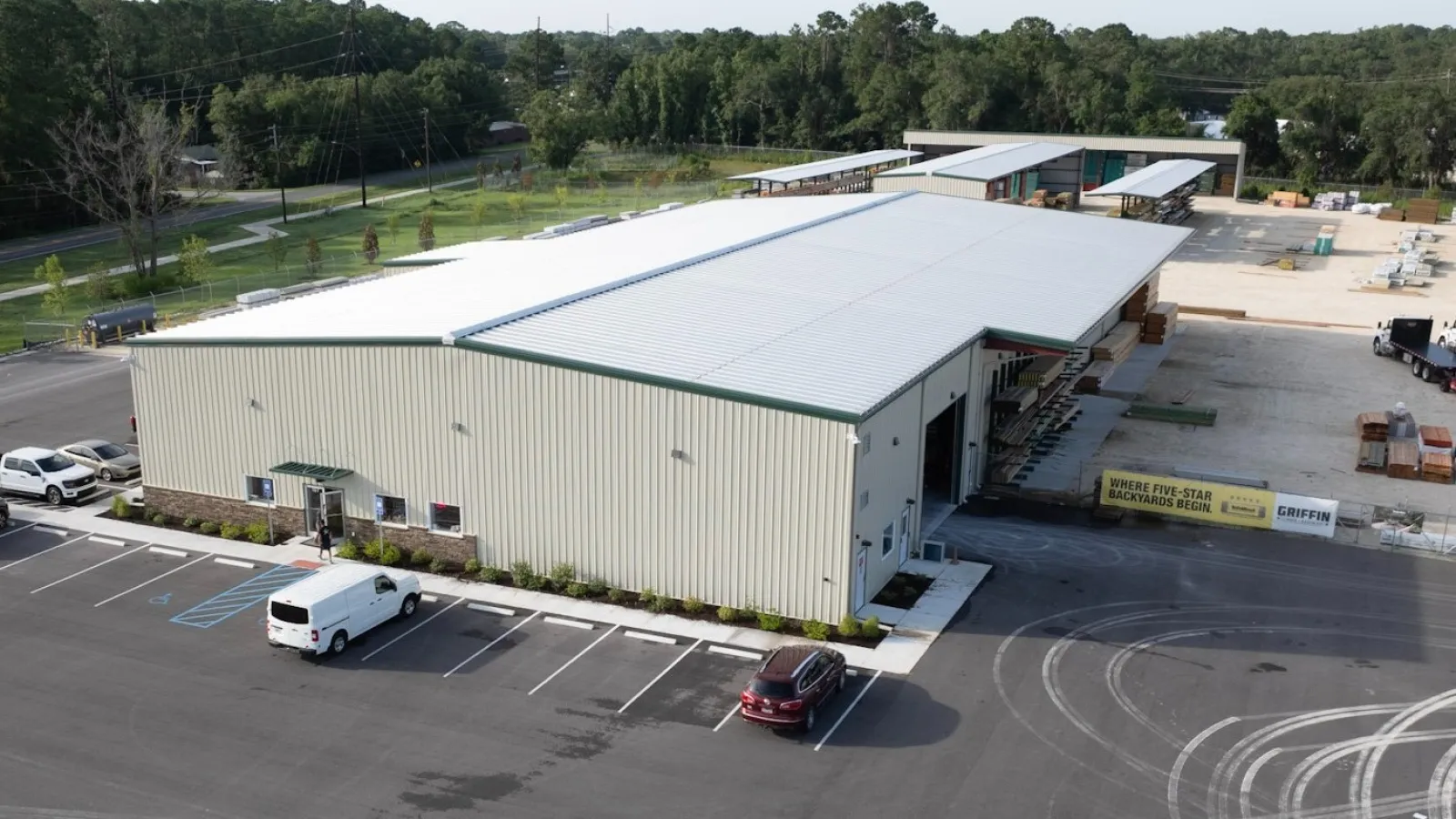 Aerial view of a large industrial warehouse with parking lot and surrounding greenery on a clear day