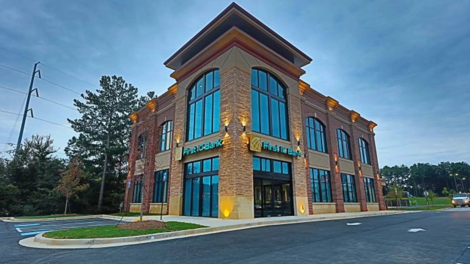 Modern two-story First TC Bank building with large windows at dusk and surrounding parking lot