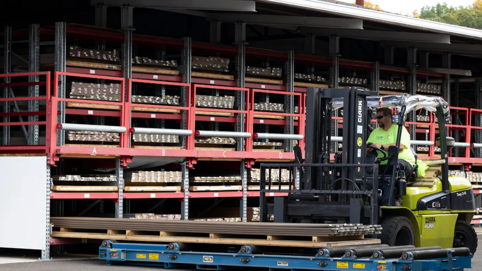 Warehouse forklift operator transporting long metal rods with organized storage racks in the background