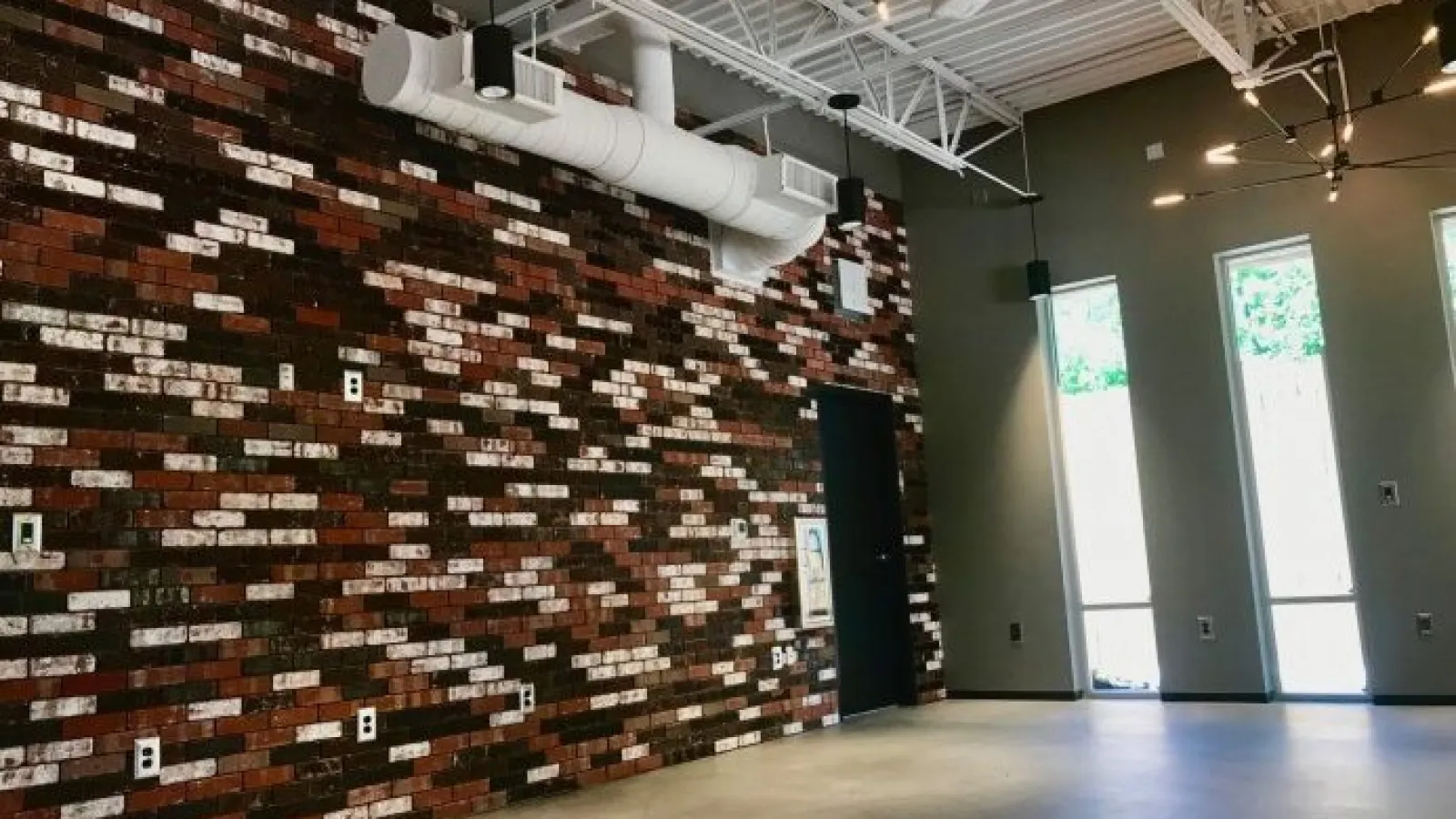 Interior space with decorative red and white brick wall, exposed white ceiling pipes, and tall windows letting in natural light