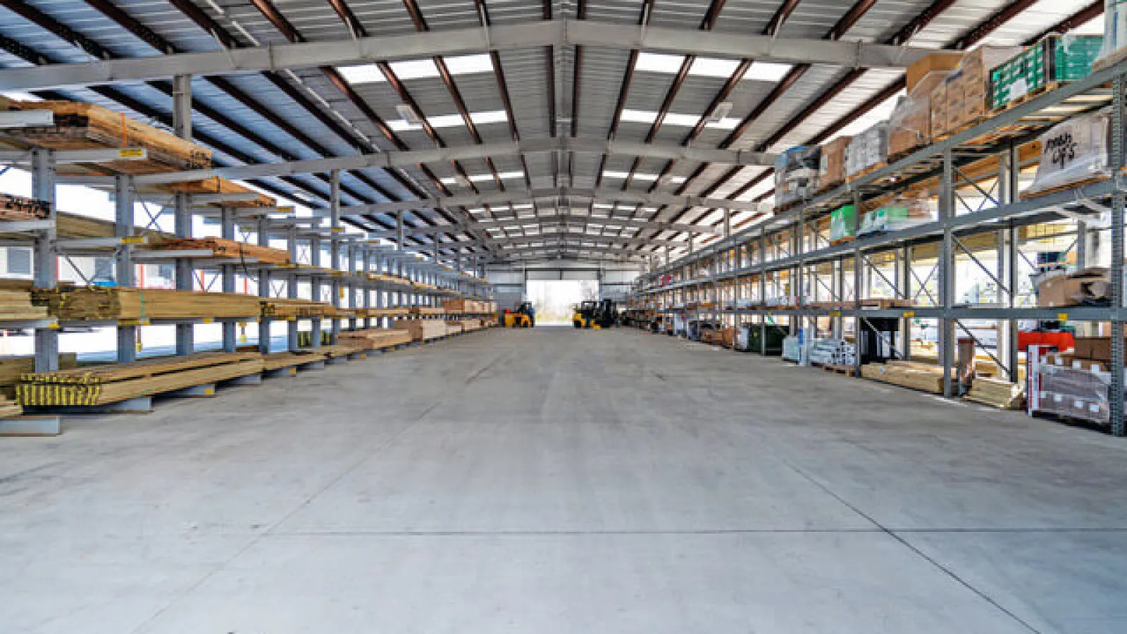 Spacious warehouse interior with metal racks storing wood and building materials under a high ceiling
