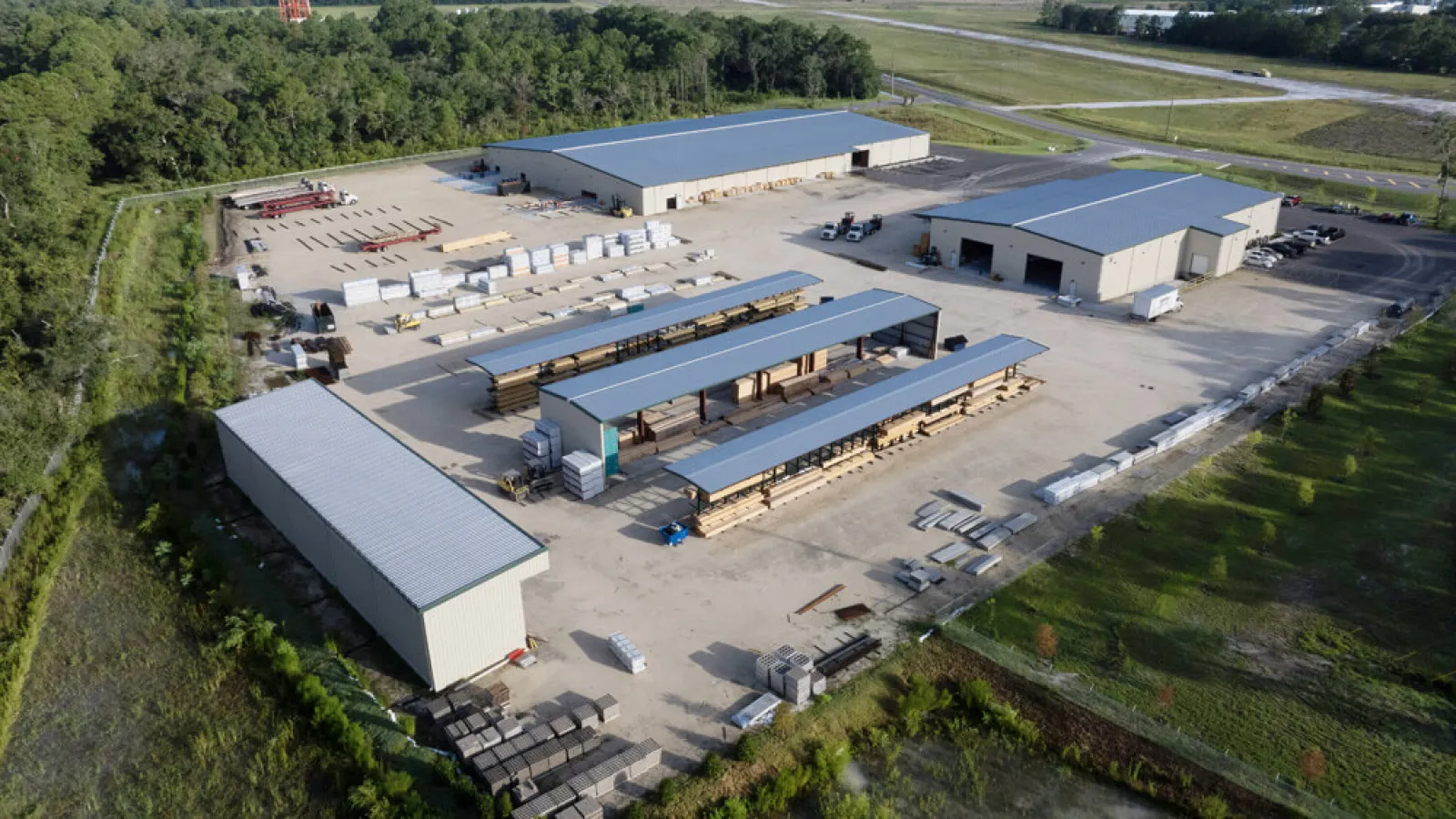 Aerial view of an industrial lumber yard with covered storage racks and multiple warehouse buildings.