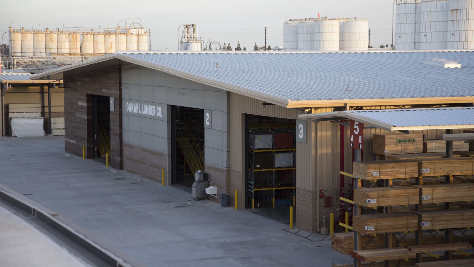 Ganahl Lumber Co outdoor storage with stacks of lumber and industrial tanks in background on a sunny day