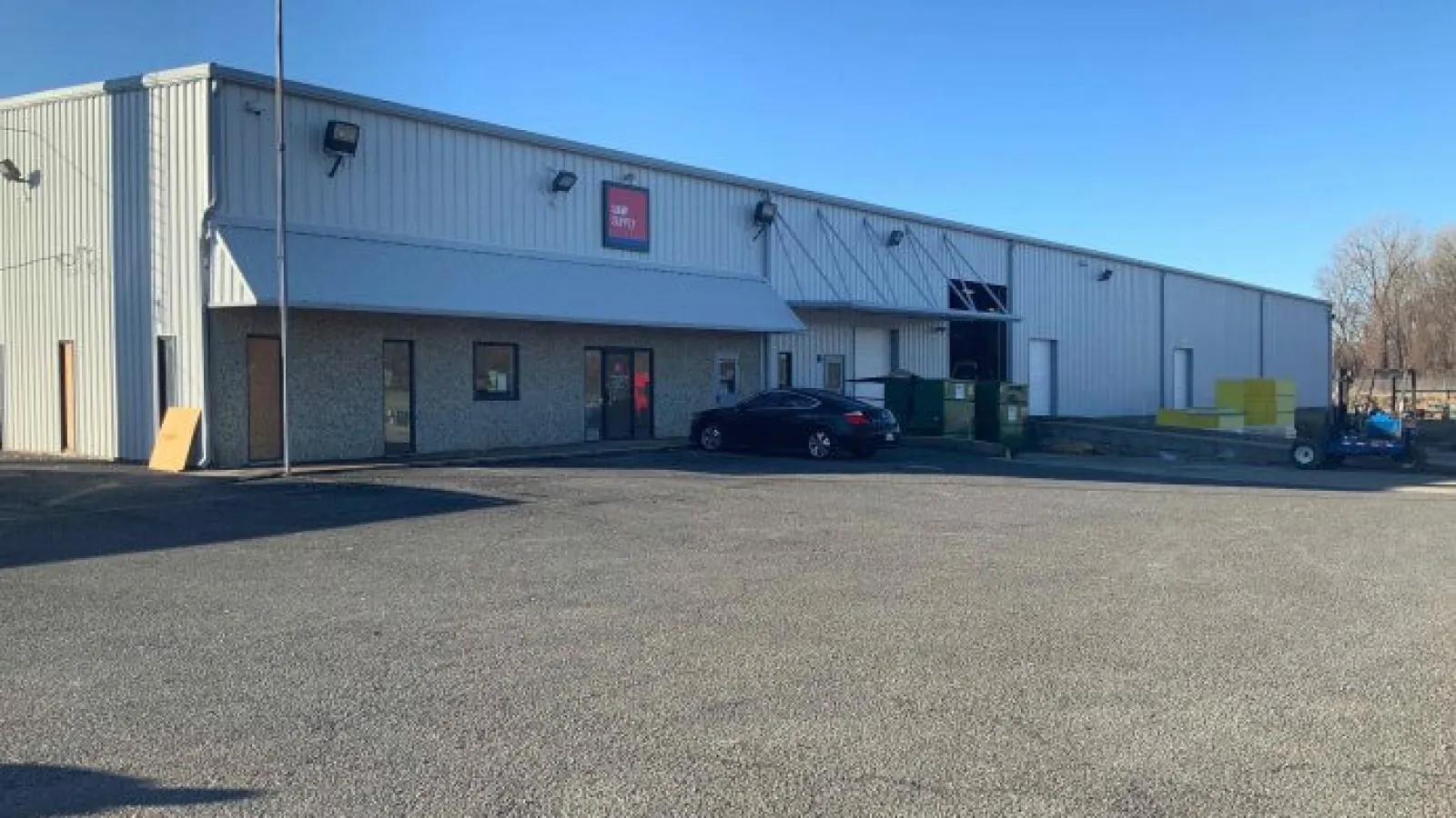Industrial warehouse building with metal siding, parking area, and a black car near the entrance on a clear day