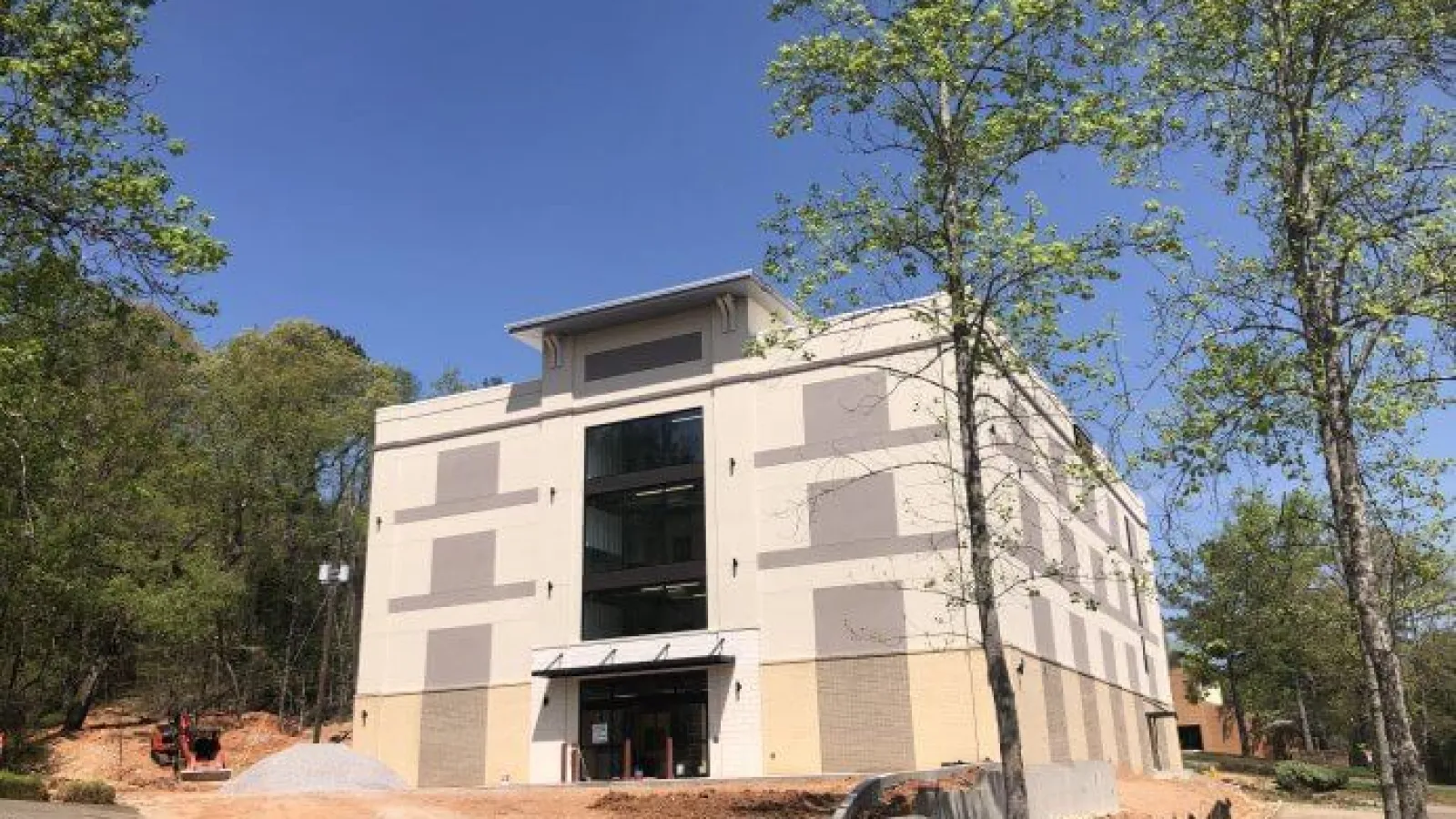 Modern beige multi-story building under construction surrounded by trees and clear blue sky.