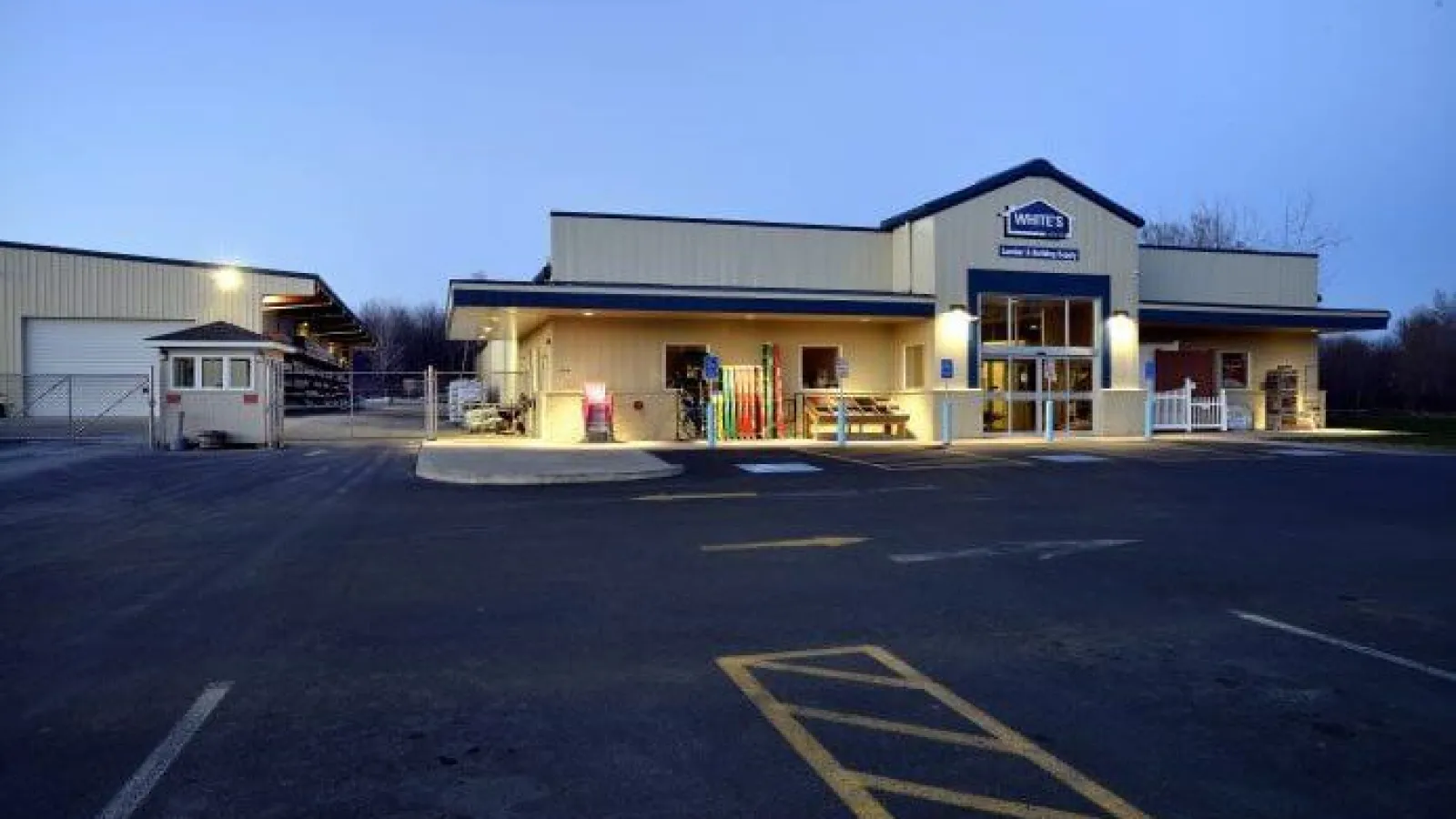Exterior view of a hardware store building illuminated at dusk with an empty parking lot in front