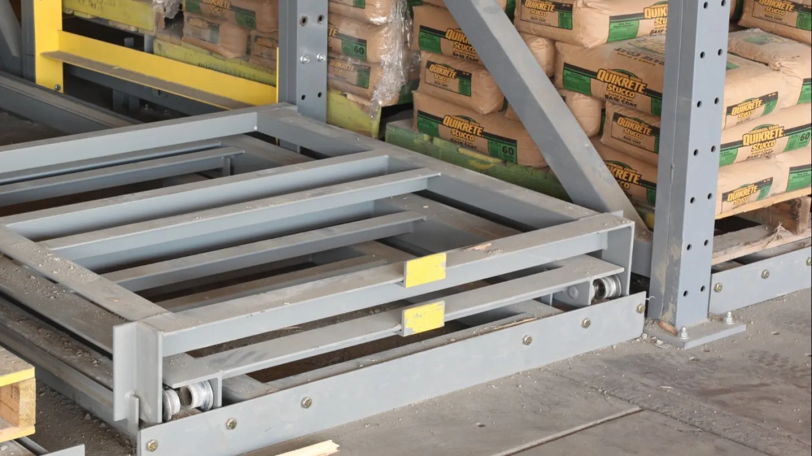 Warehouse storage with pallets of cement bags and a metal roller conveyor system on concrete floor.
