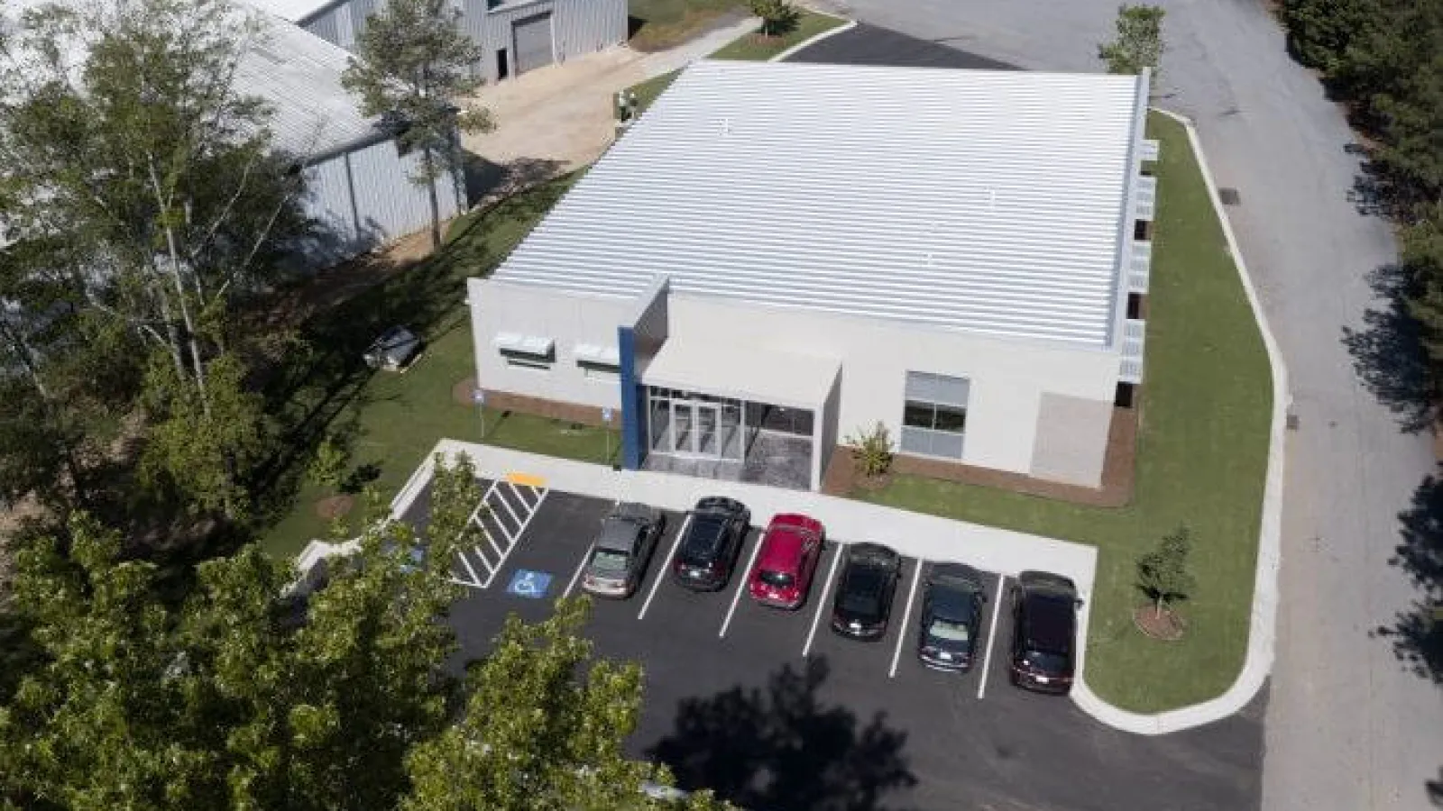 Aerial view of a modern single-story commercial building with adjacent parking lot and several parked cars.