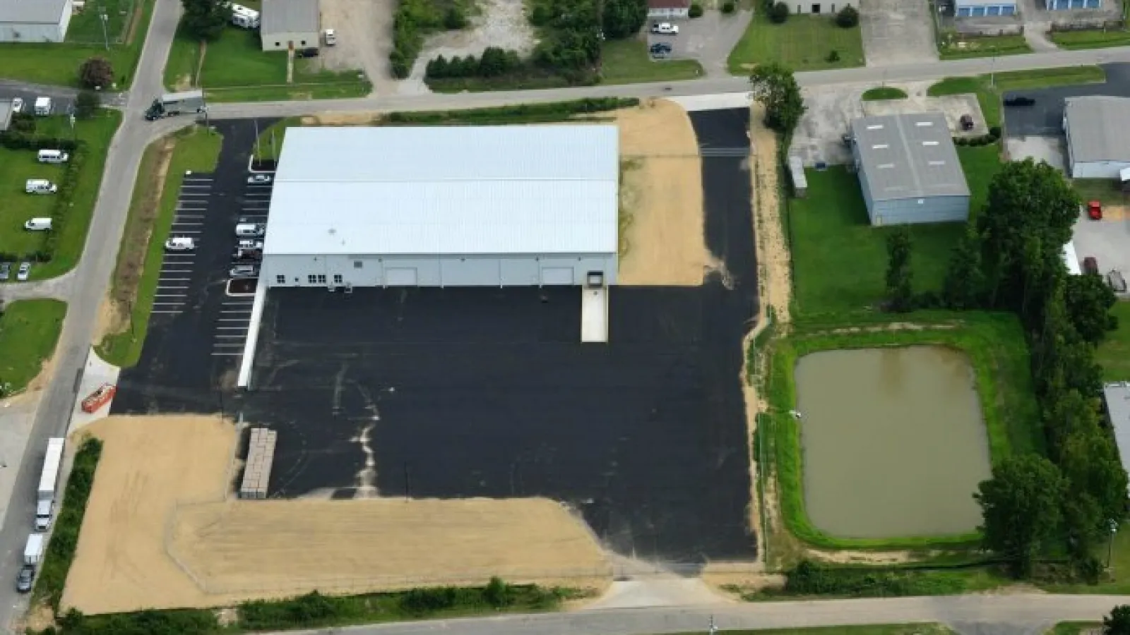 Aerial view of a large warehouse with a new blacktop parking lot and adjacent water pond in an industrial area.
