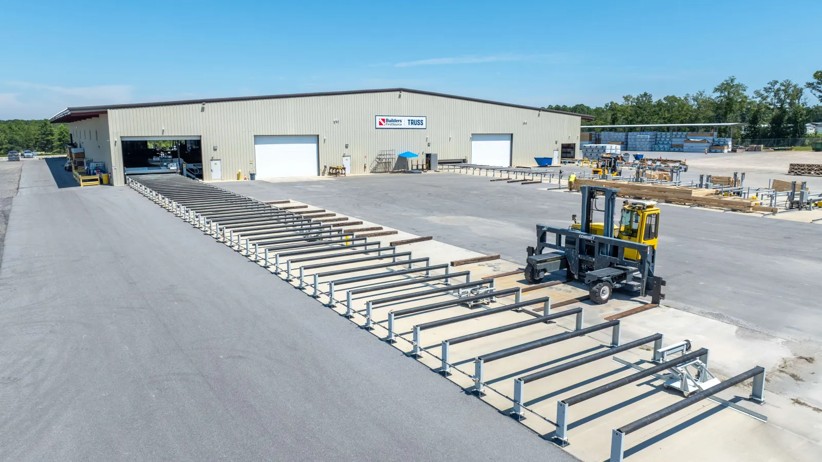 Industrial yard with metal framework, forklift, and warehouse building under clear blue sky