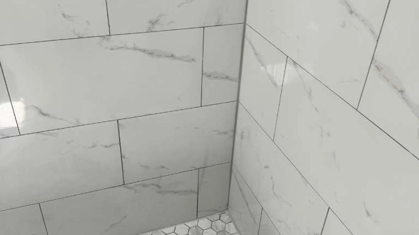 Shower corner with large marble-effect rectangular wall tiles and small hexagonal floor tiles in gray tones.
