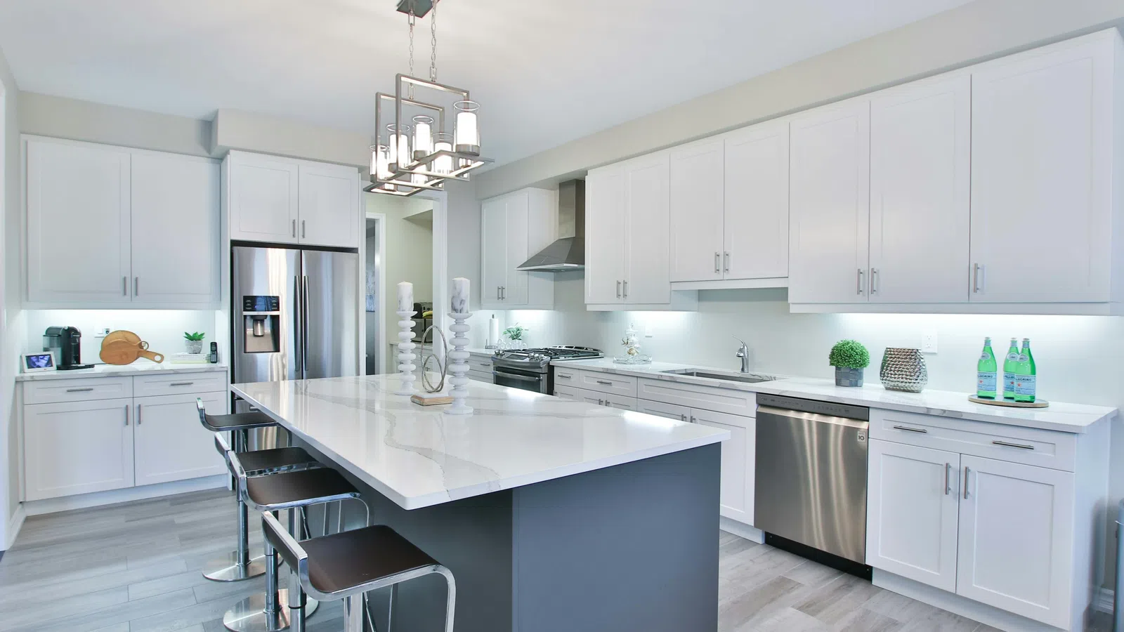 Modern kitchen with white cabinetry, marble island, stainless steel appliances, and gray flooring under bright lighting