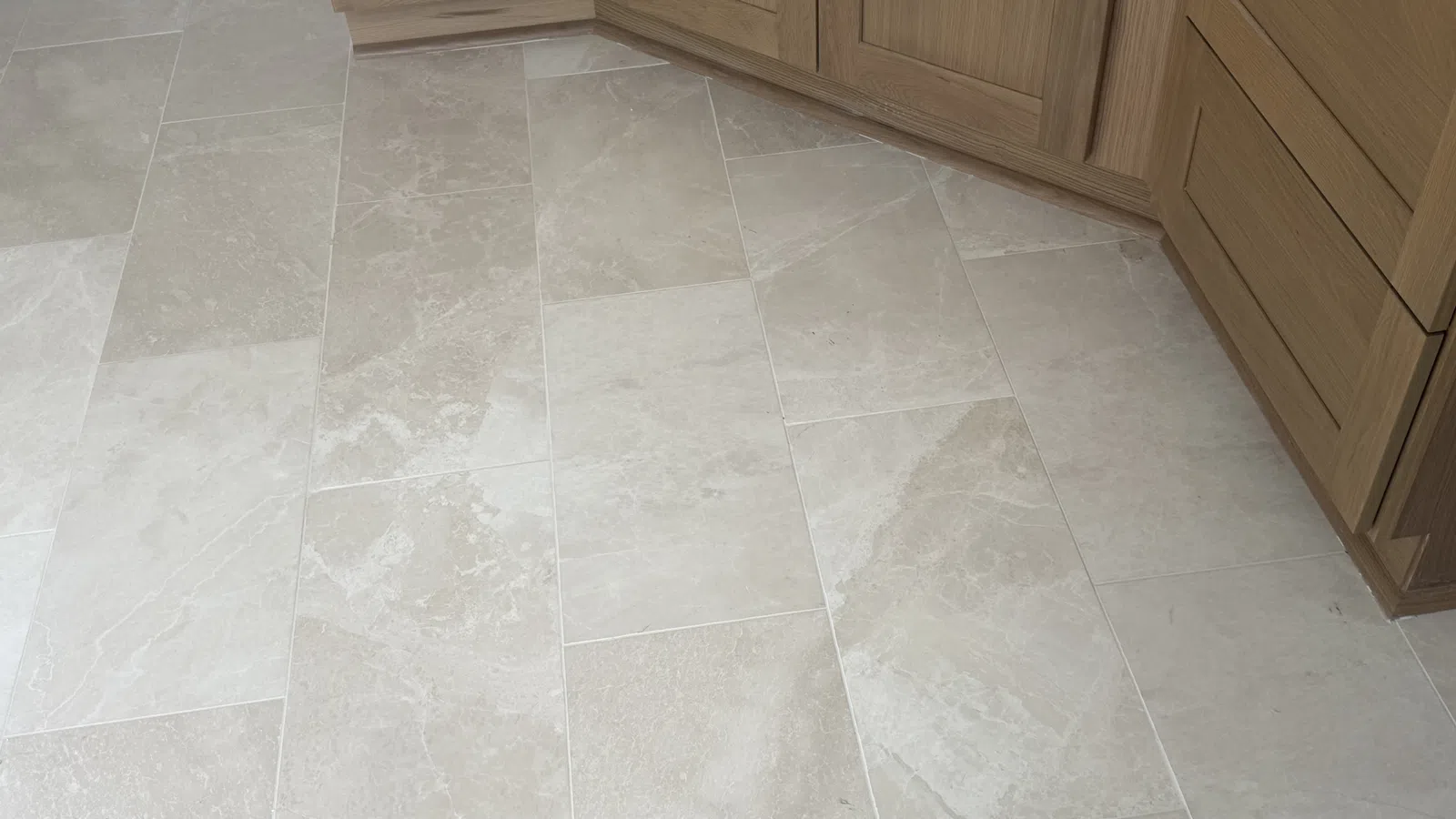 Beige stone tile floor with varied natural patterns under wooden kitchen cabinets with drawers and doors.