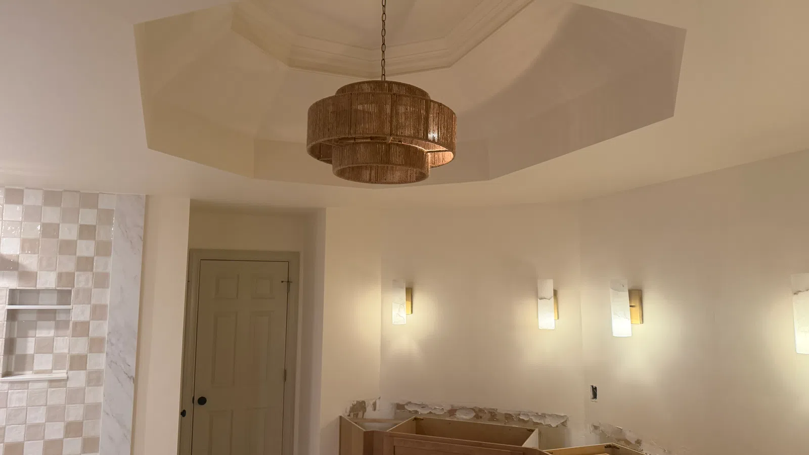 Partially renovated bathroom with wood cabinets, beige walls, mosaic tile shower, and a tiered pendant light fixture
