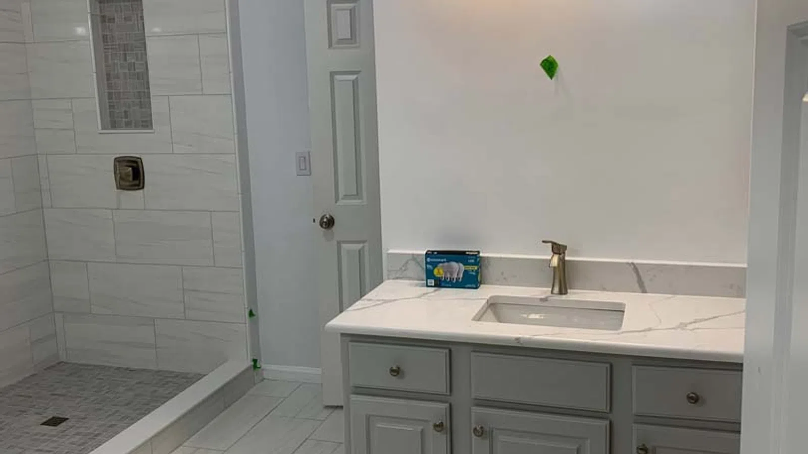 Modern bathroom with gray vanity, white countertop, built-in shower with tiled walls and floor, and overhead lighting.