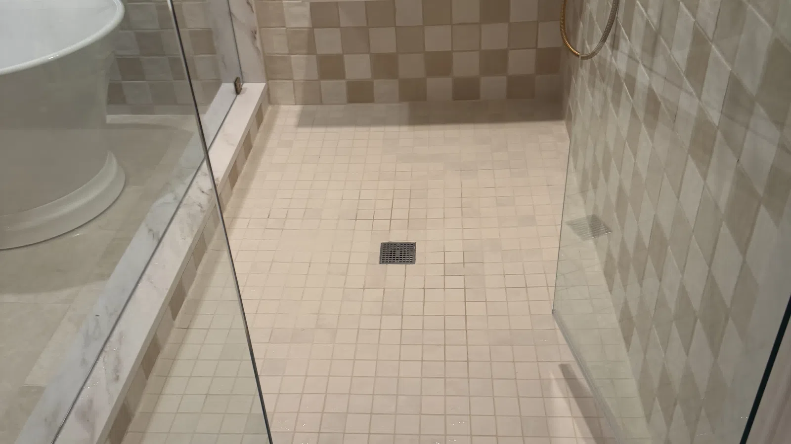 Modern walk-in shower with glass door, beige checkered tile walls, built-in bench, and bathroom products.