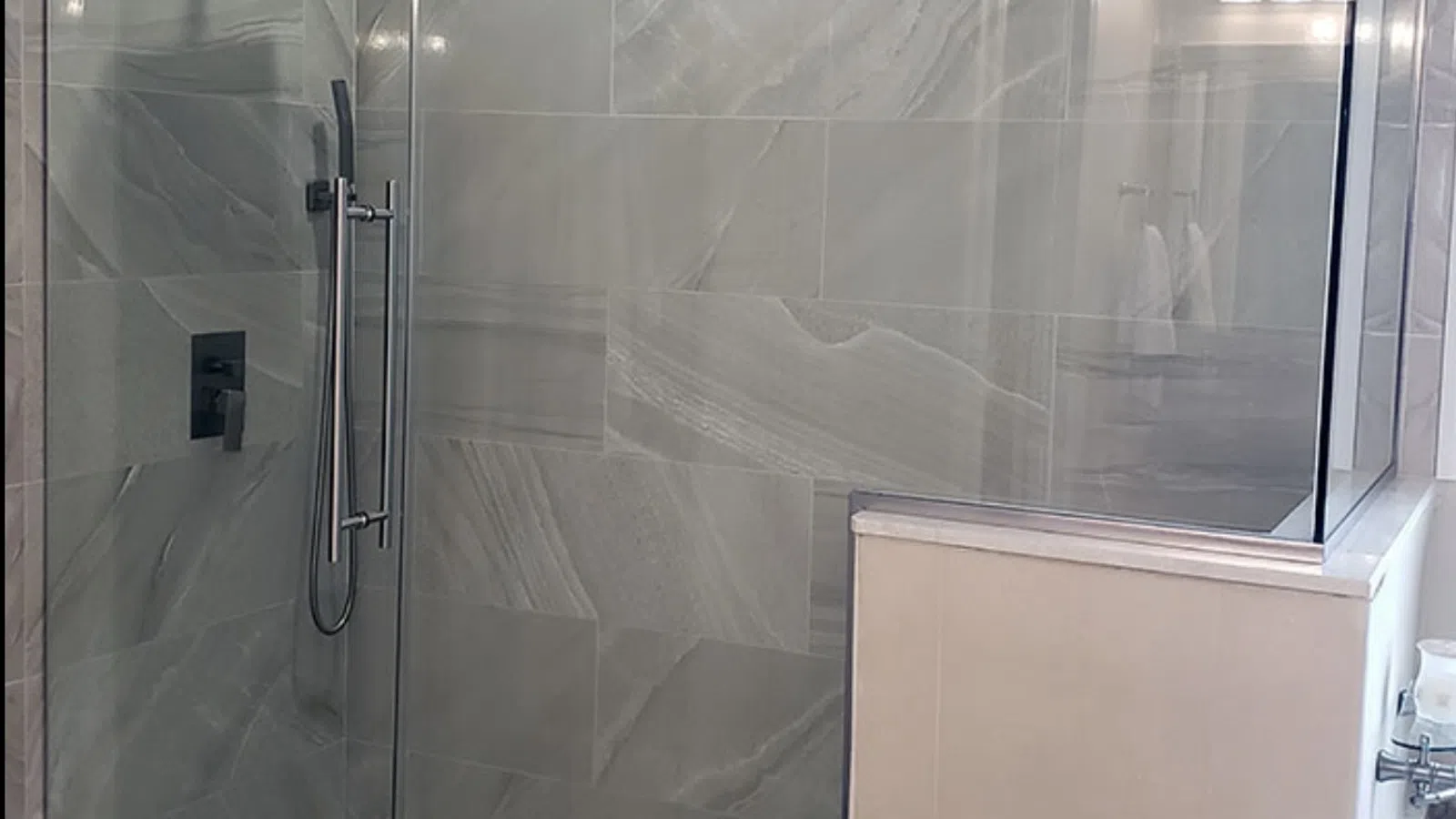 Modern walk-in shower with glass enclosure, gray marble tiles, pebble stone floor, and rain showerhead.