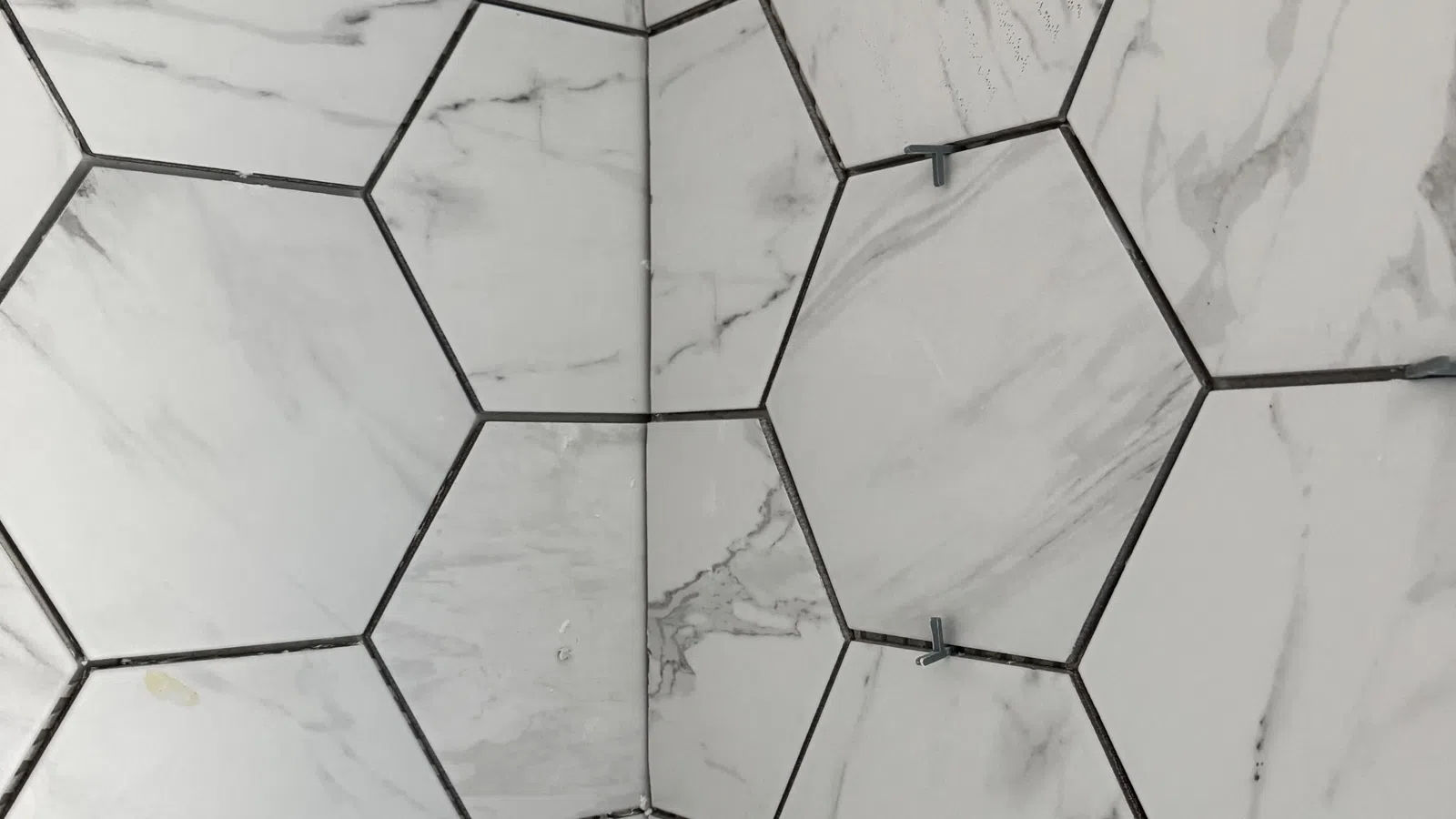Close-up of marble hexagonal tiles installed on a wall with spacers between grout lines.