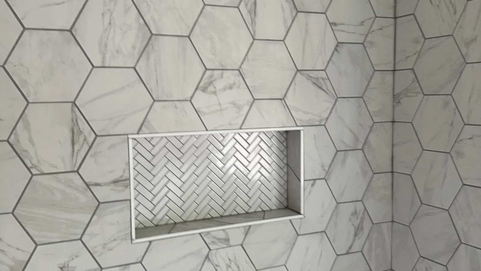 Bathroom wall with large hexagonal marble tiles and inset shelf with herringbone pattern tiles.