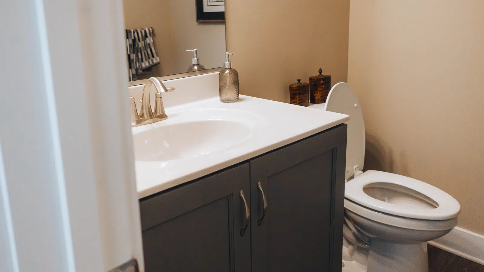 Modern bathroom with white toilet, gray vanity cabinet, sink with faucet, and beige walls.