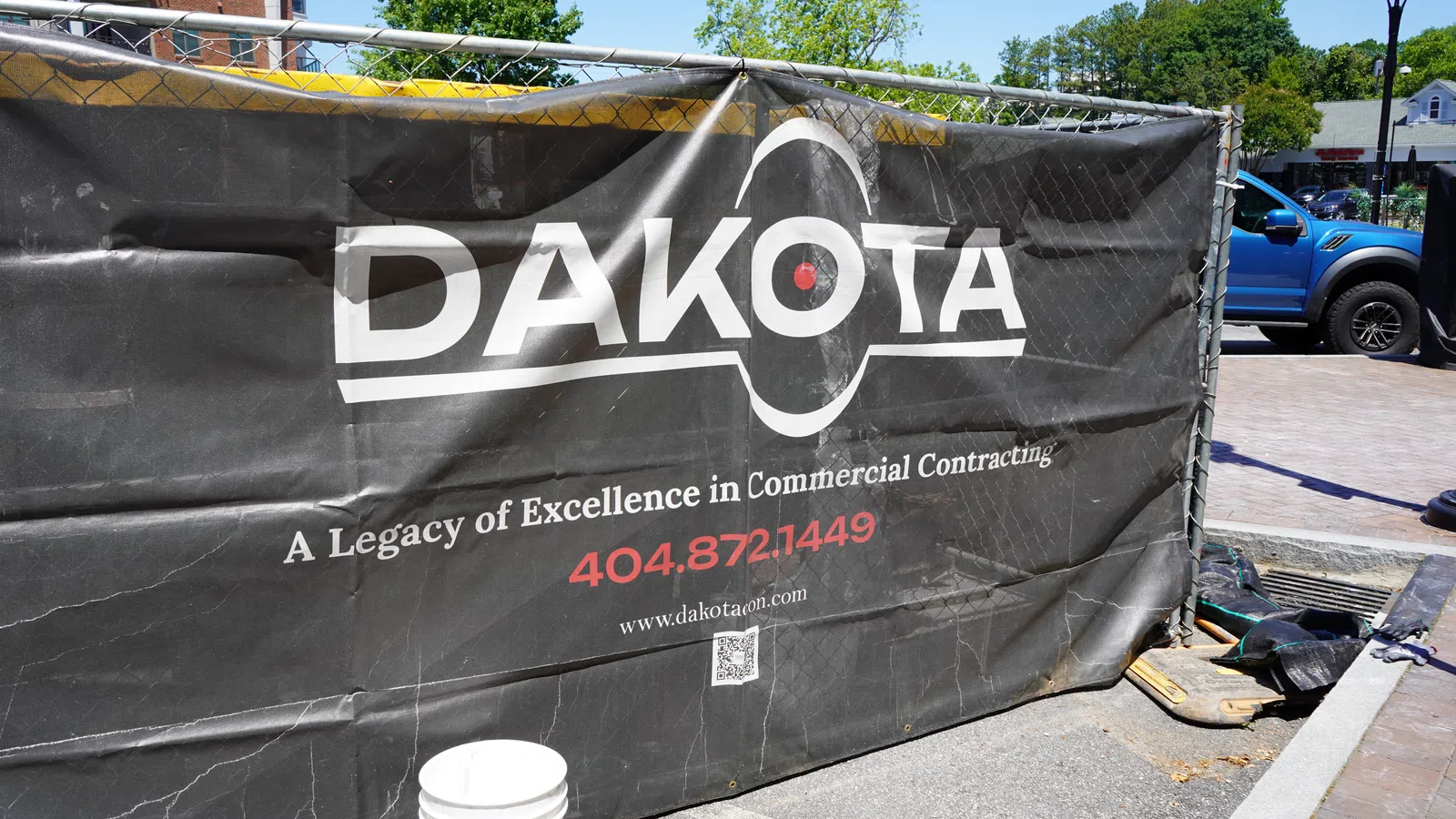 Black Dakota construction banner on chain link fence with commercial contracting contact info outdoors.