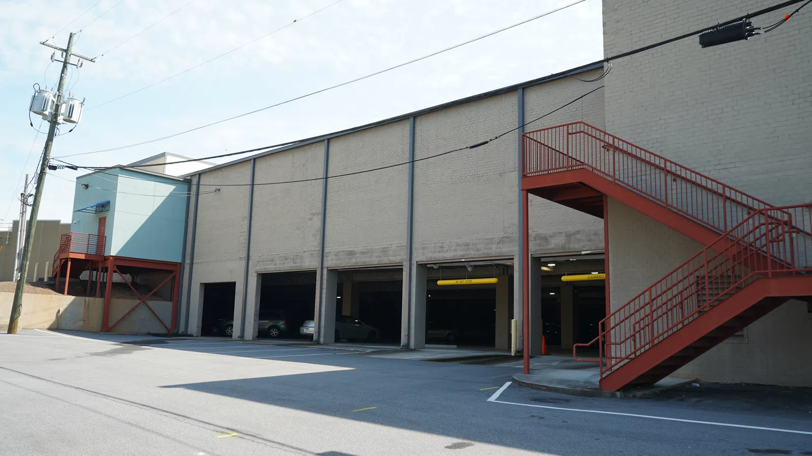 Empty urban parking garage with several open bays and red metal exterior staircases on a sunny day.