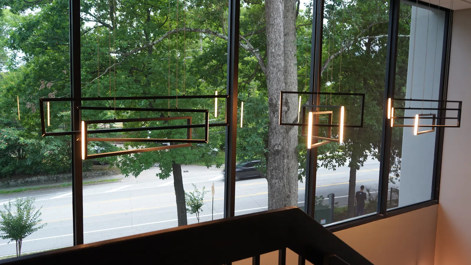Modern geometric pendant lights hanging in front of large windows overlooking a tree-lined street.