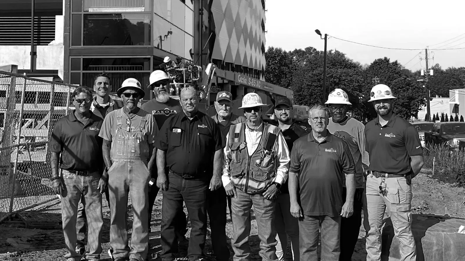 Construction workers posing together on a building site with modern building and equipment in background