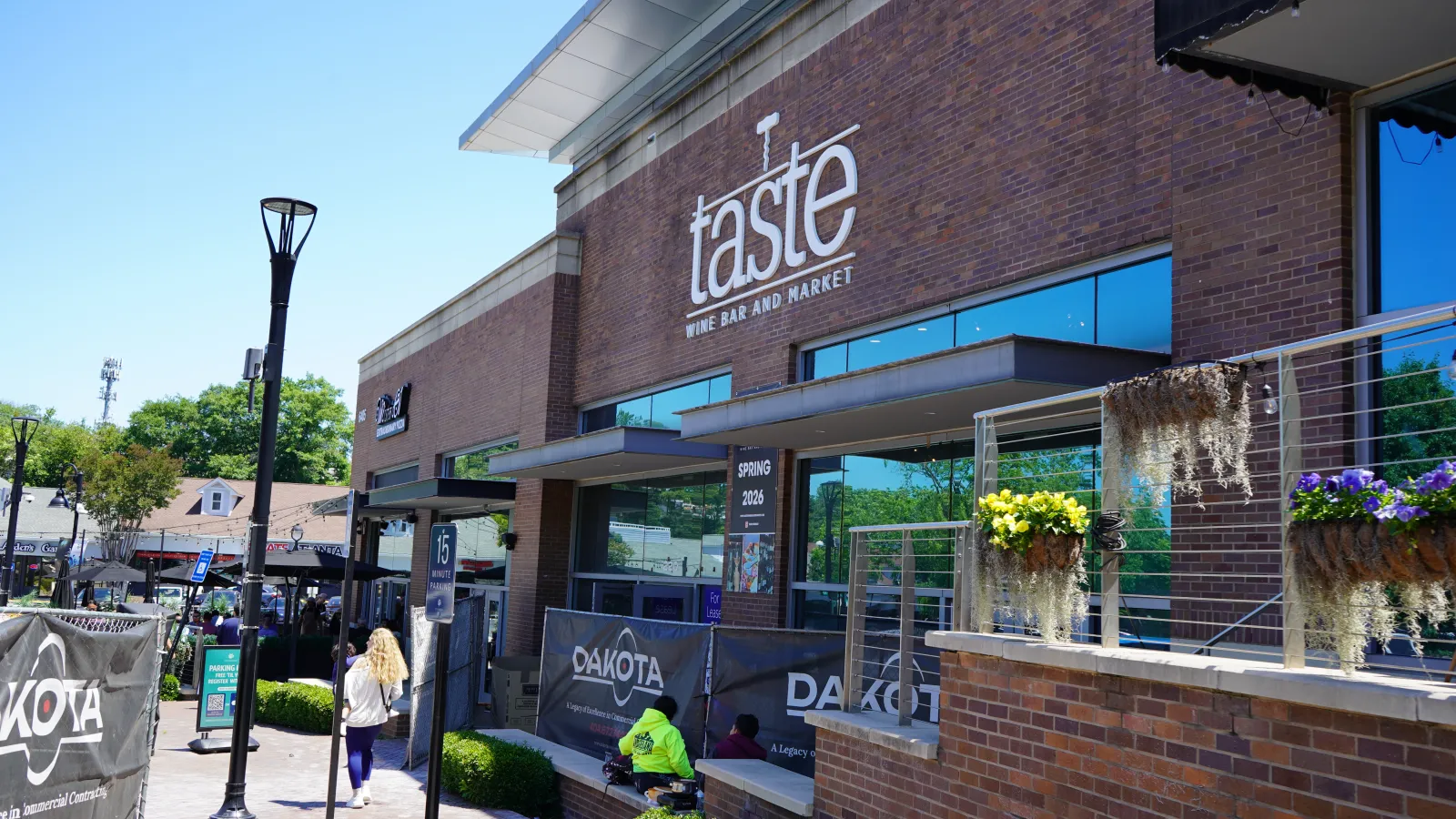 Taste Wine Bar and Market exterior with outdoor seating, brick facade, and flower planters under clear blue sky.