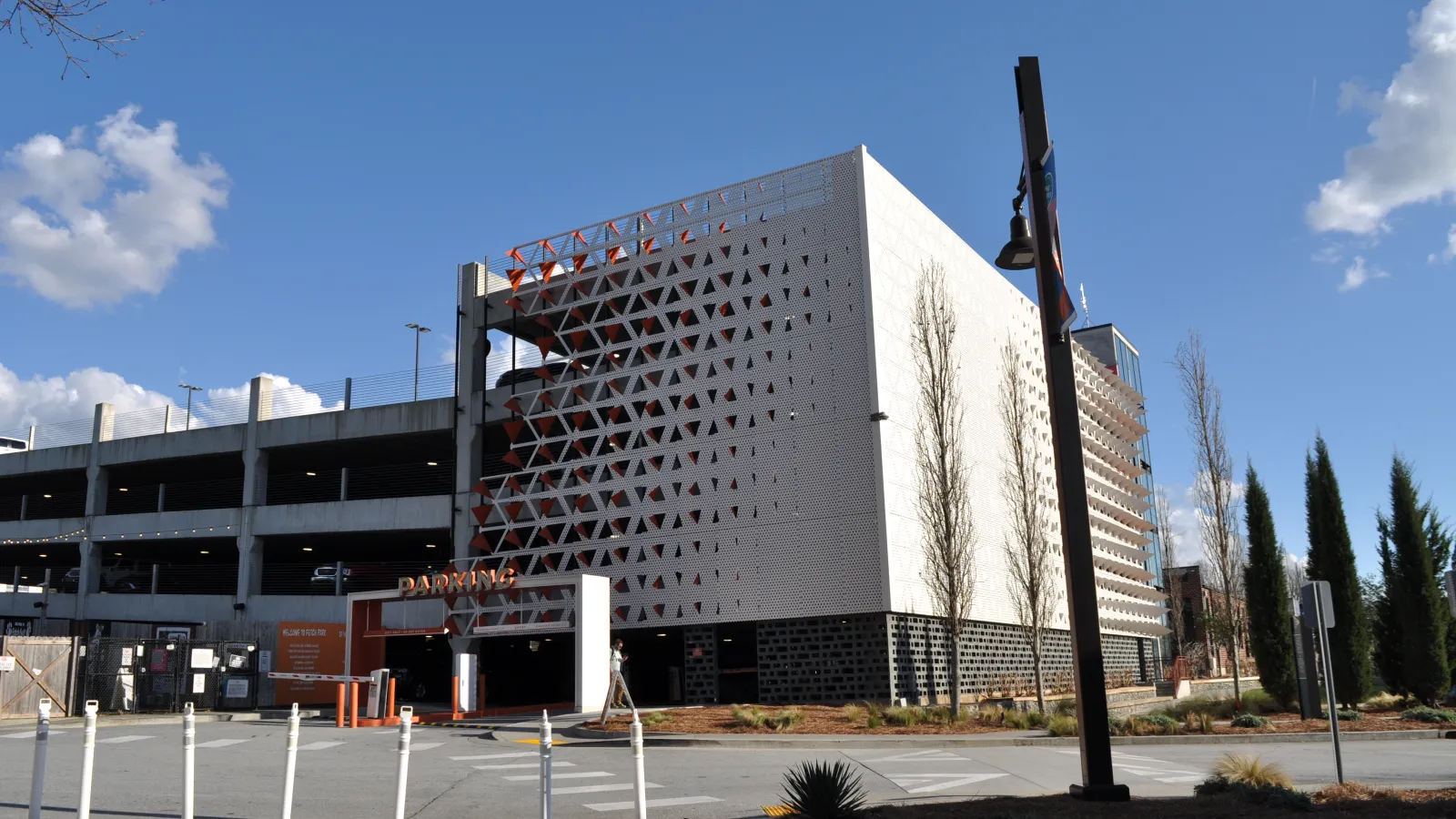 Modern multi-level parking garage with geometric facade under clear blue sky with scattered clouds.
