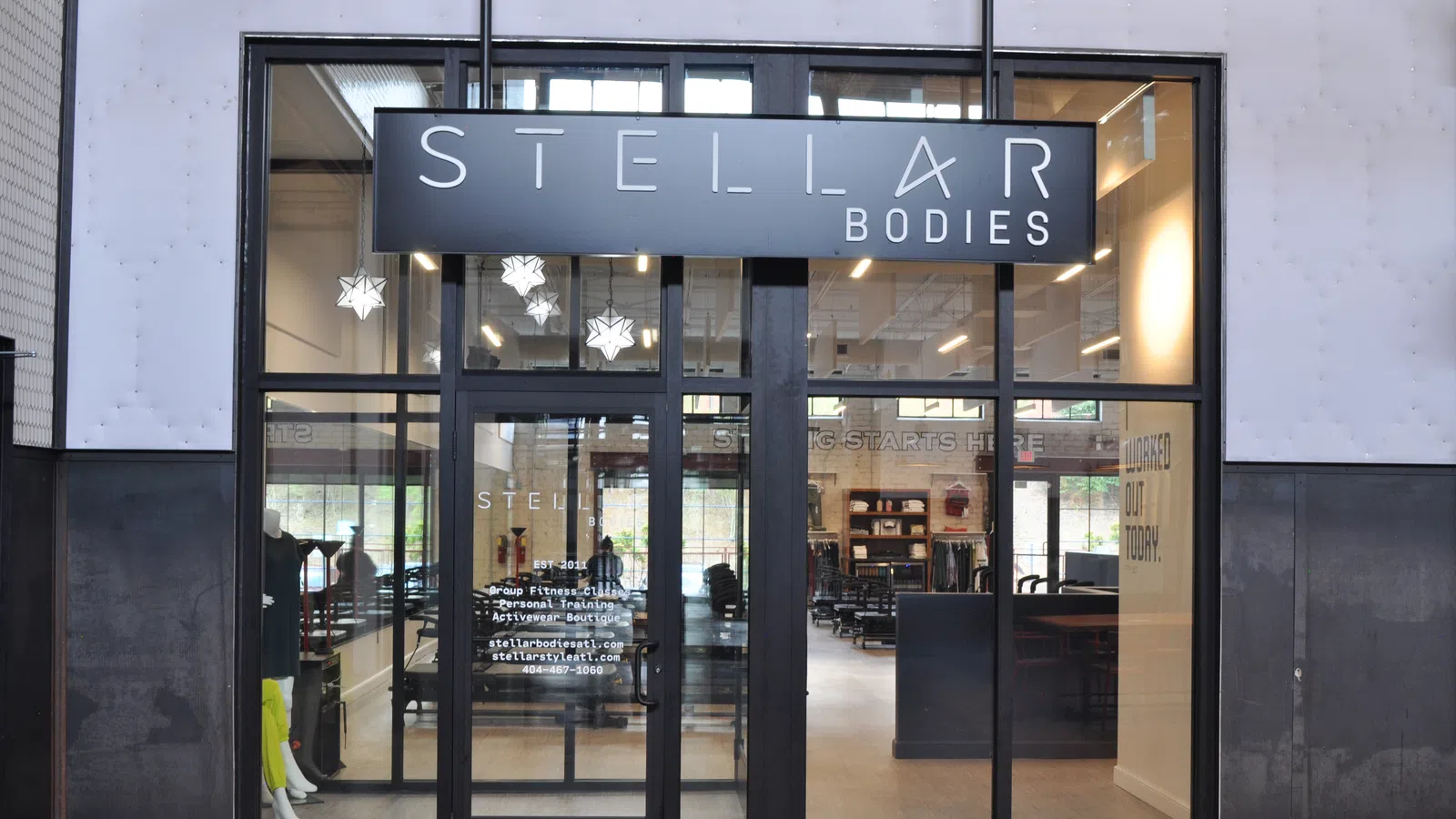 Modern storefront of Stellar Bodies gym with glass doors, visible workout equipment, and hanging star lights.