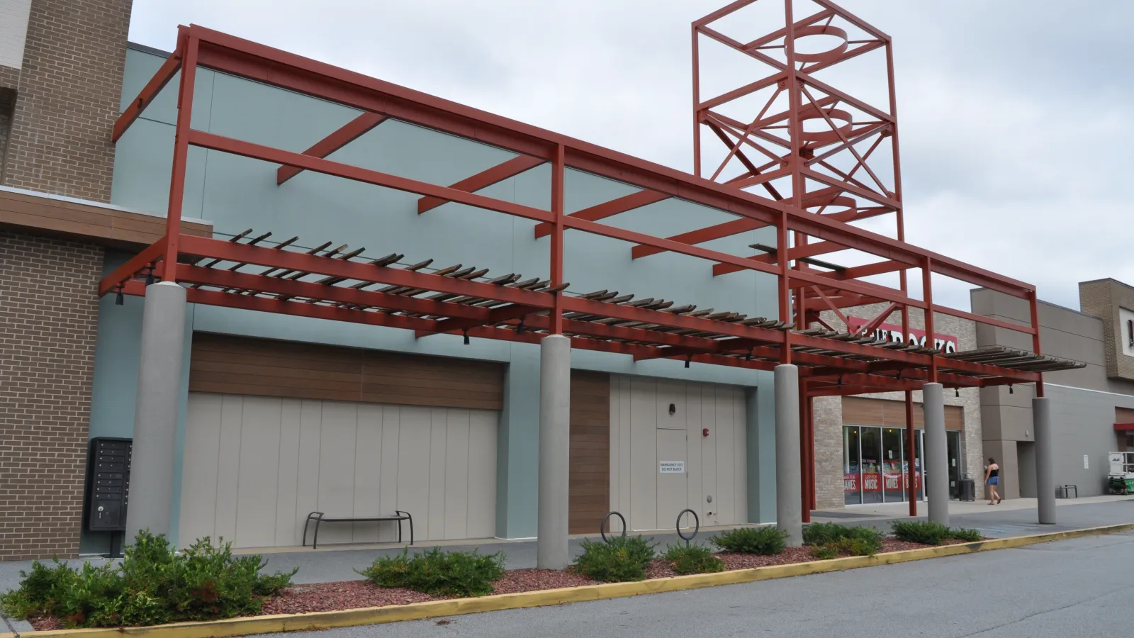 Empty storefront with modern red metal awning structure and overcast sky in a shopping center parking lot