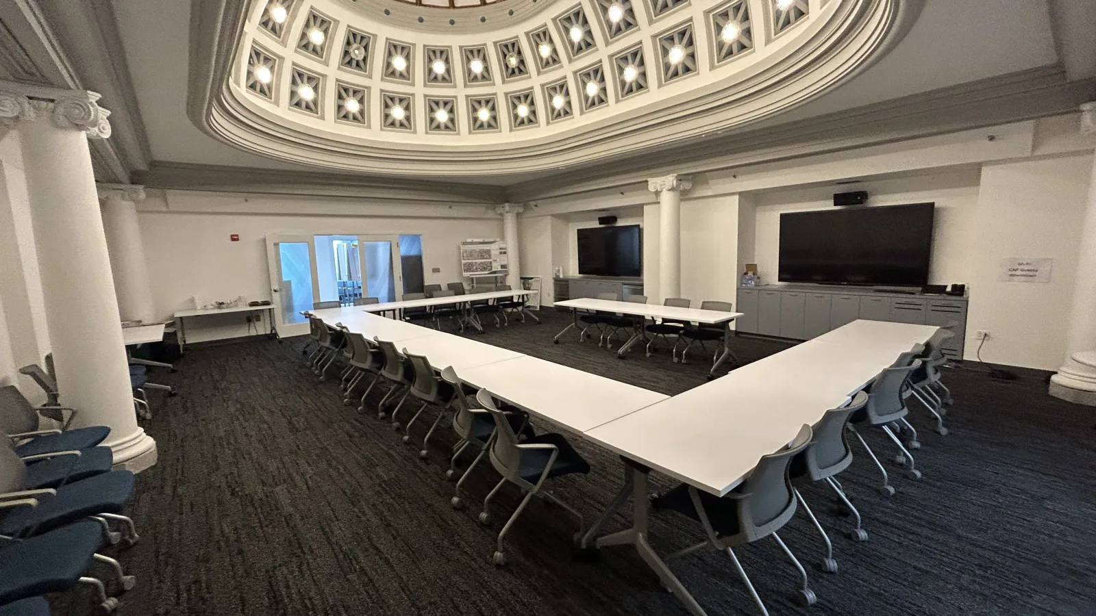 Conference room with U-shaped tables and chairs under a decorative domed ceiling with natural light.