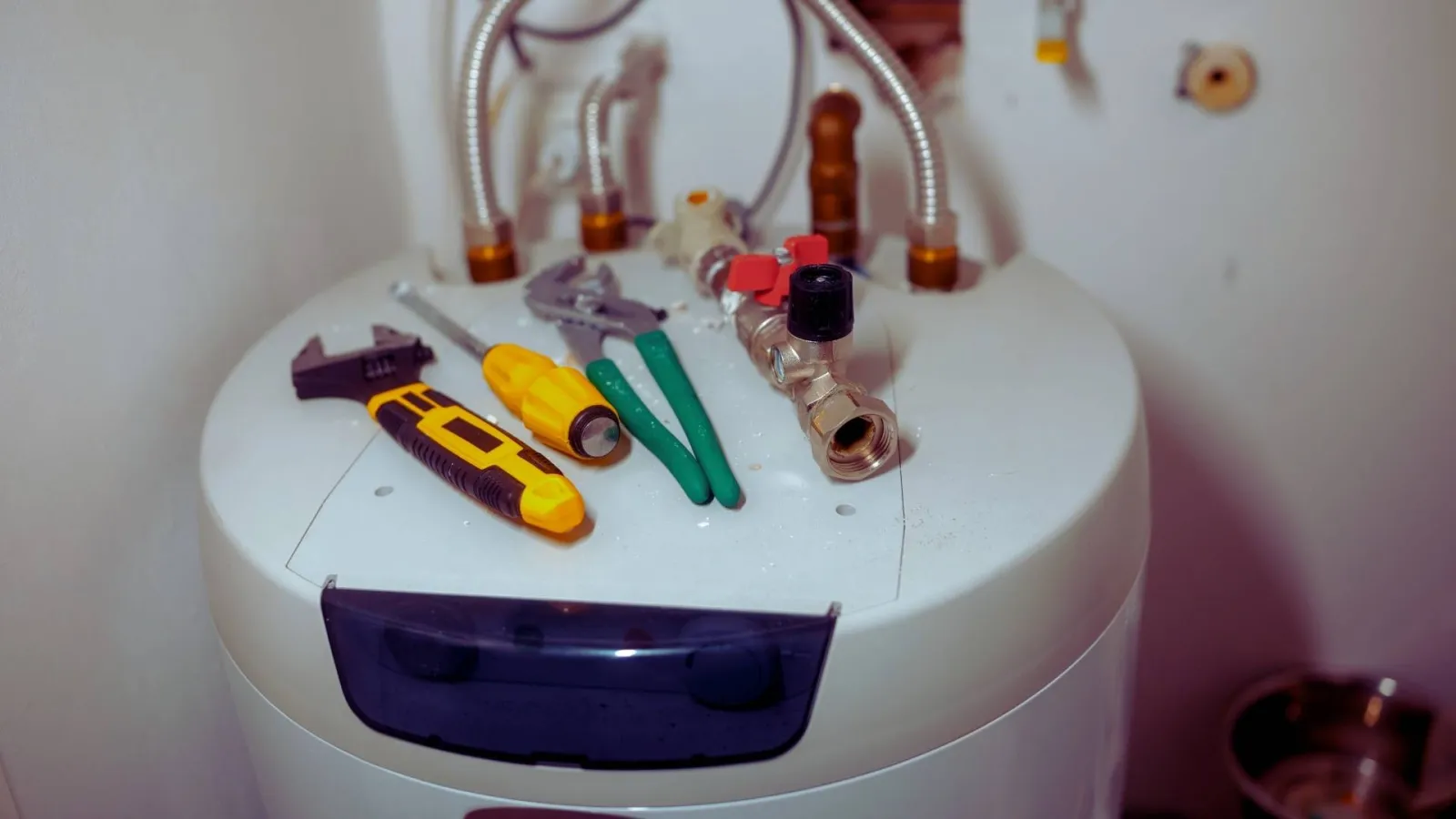 Plumbing tools including wrench, screwdriver, and pliers on top of a white water heater in a utility area.