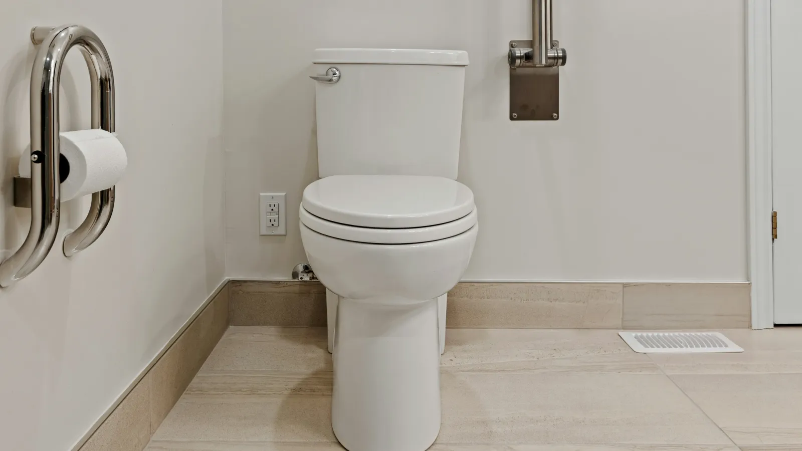 Modern white toilet with stainless steel grab bars and tiled floor in accessible bathroom corner.