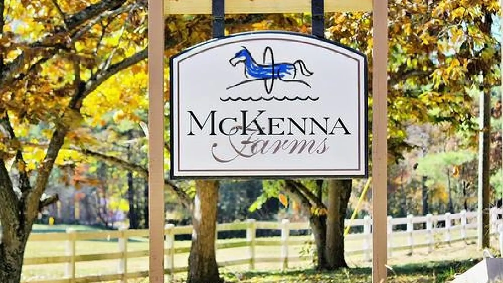McKenna Farms sign with a blue horse logo hanging between wooden posts in a fall setting