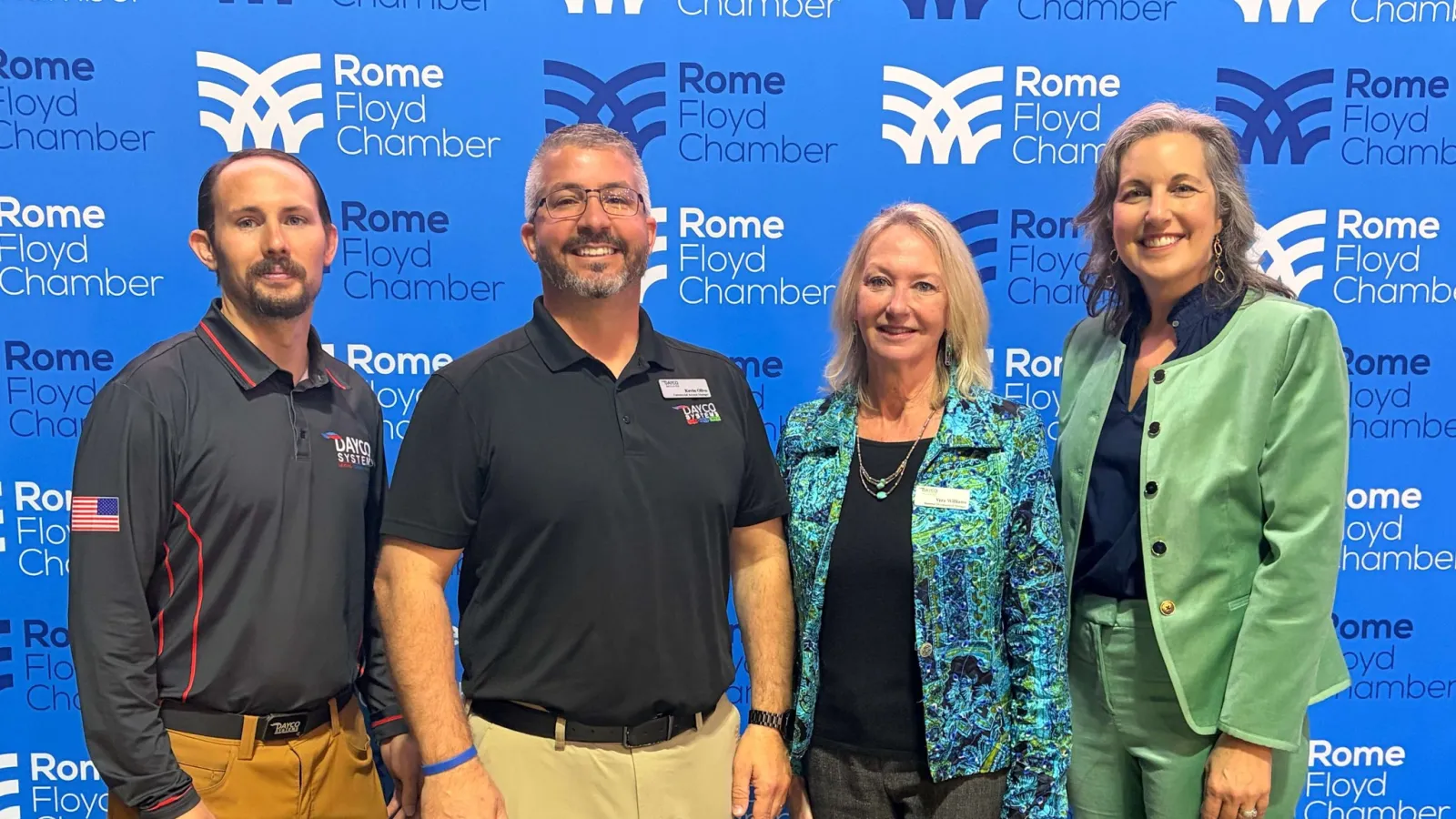 Four professionals standing in front of Rome Floyd Chamber branded blue backdrop, smiling and posing for photo